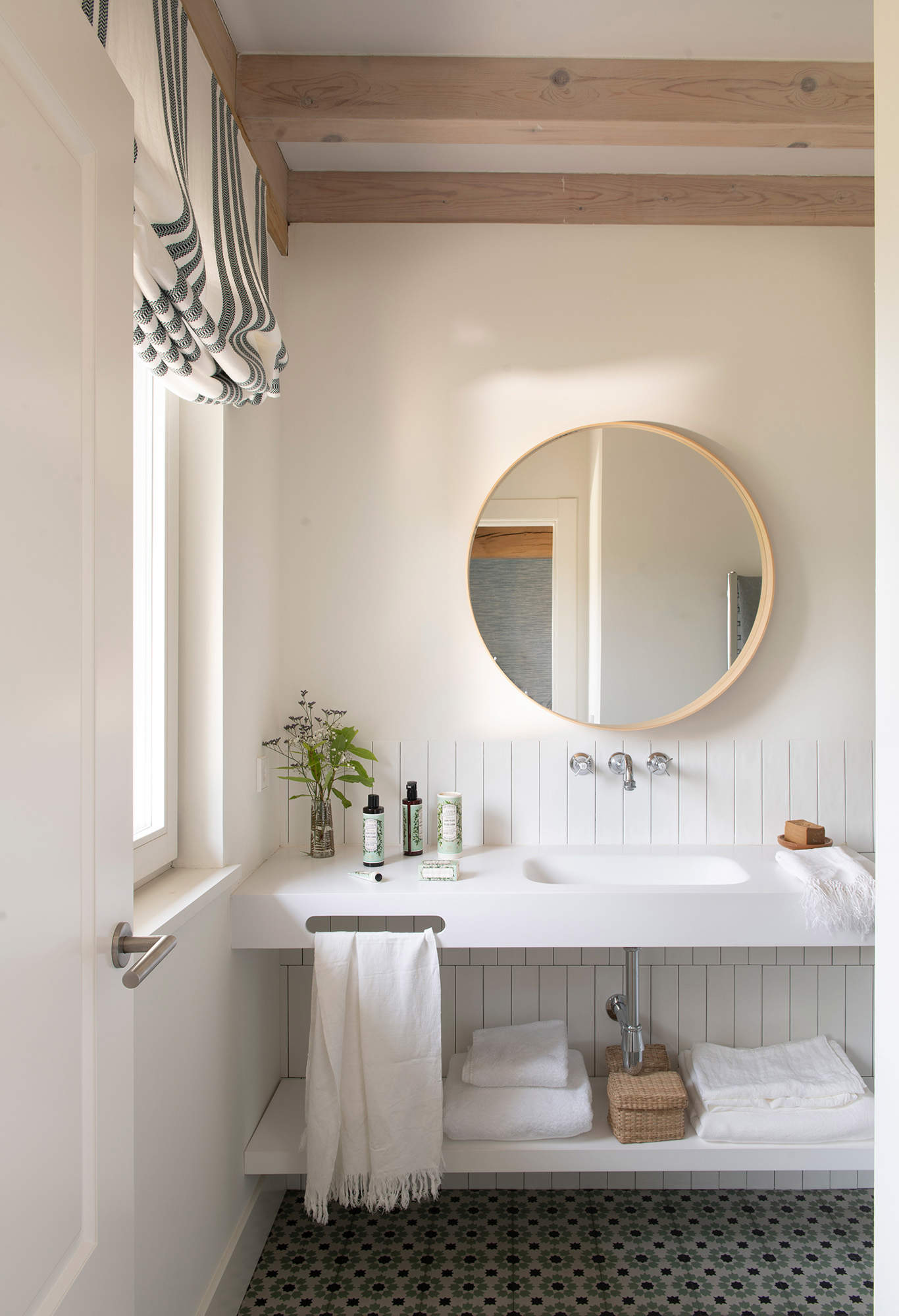 Baño con mueble de lavabo blanco y espejo redondo de madera