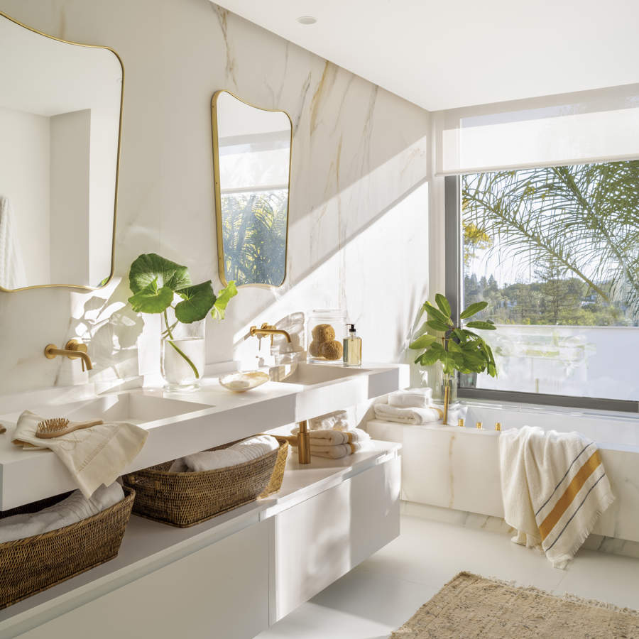 Ban~o moderno con mueble blanco volado, paredes de mármol y espejos con marco dorado