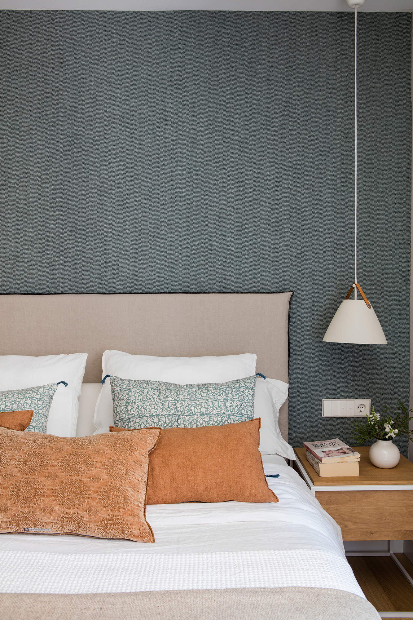 Dormitorio moderno con papel pintado en la pared y lámpara de suspensión sobre la mesilla.