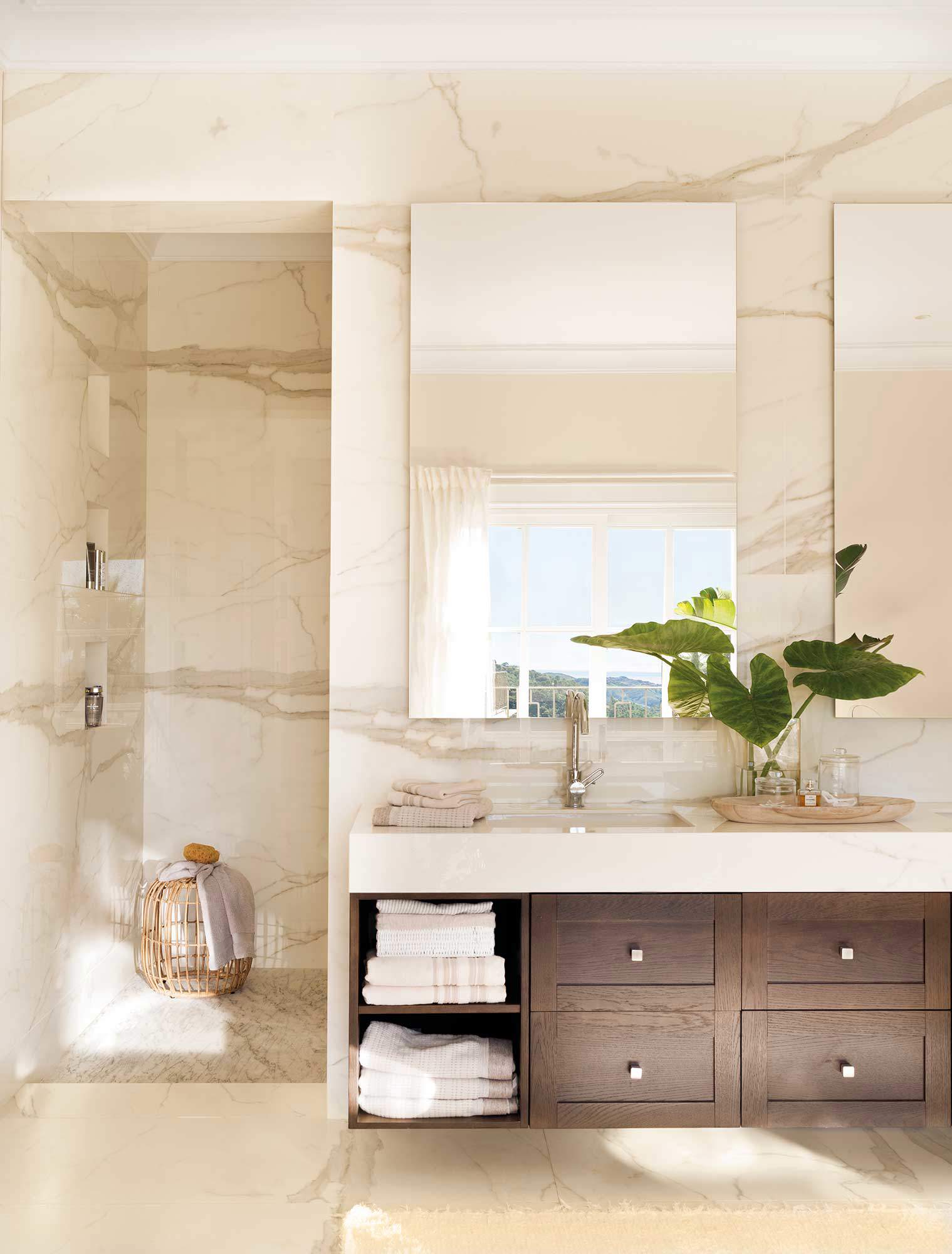 Baño revestido de mármol, mueble de madera y espejos sin marco