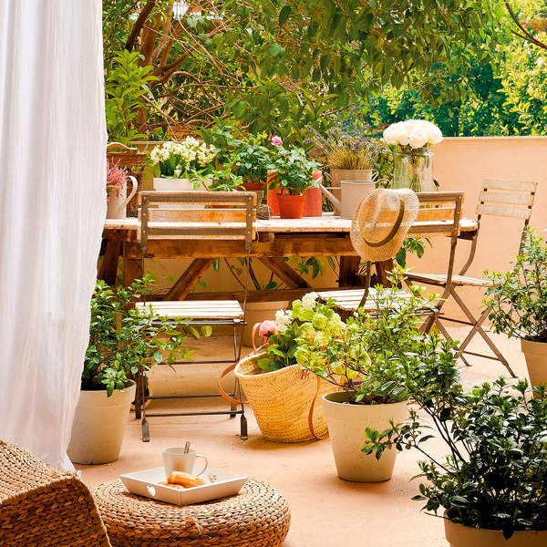 Terraza con zona de comedor, plantas en macetas de distintos tamaños y muebles de fibras naturales.