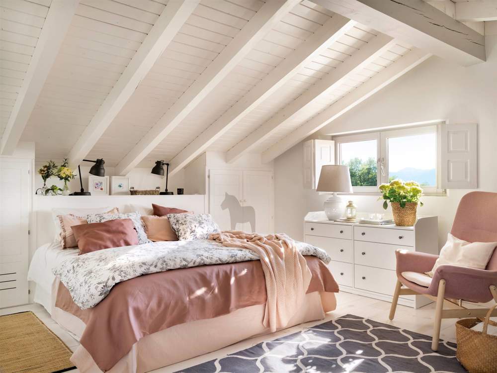 Dormitorio abuhardillado pintado en blanco con butaca rosa