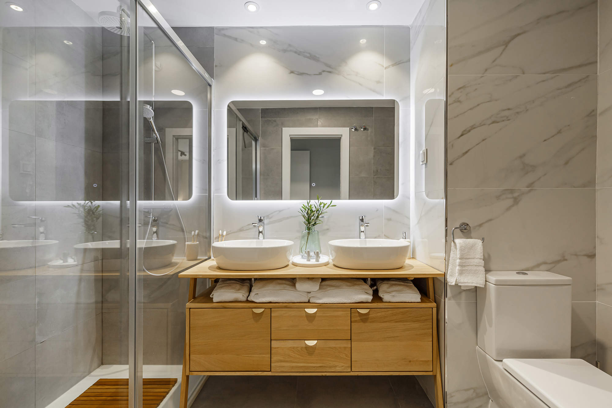 Baño con revestimientos de mármol y mueble de madera con dos lavabos