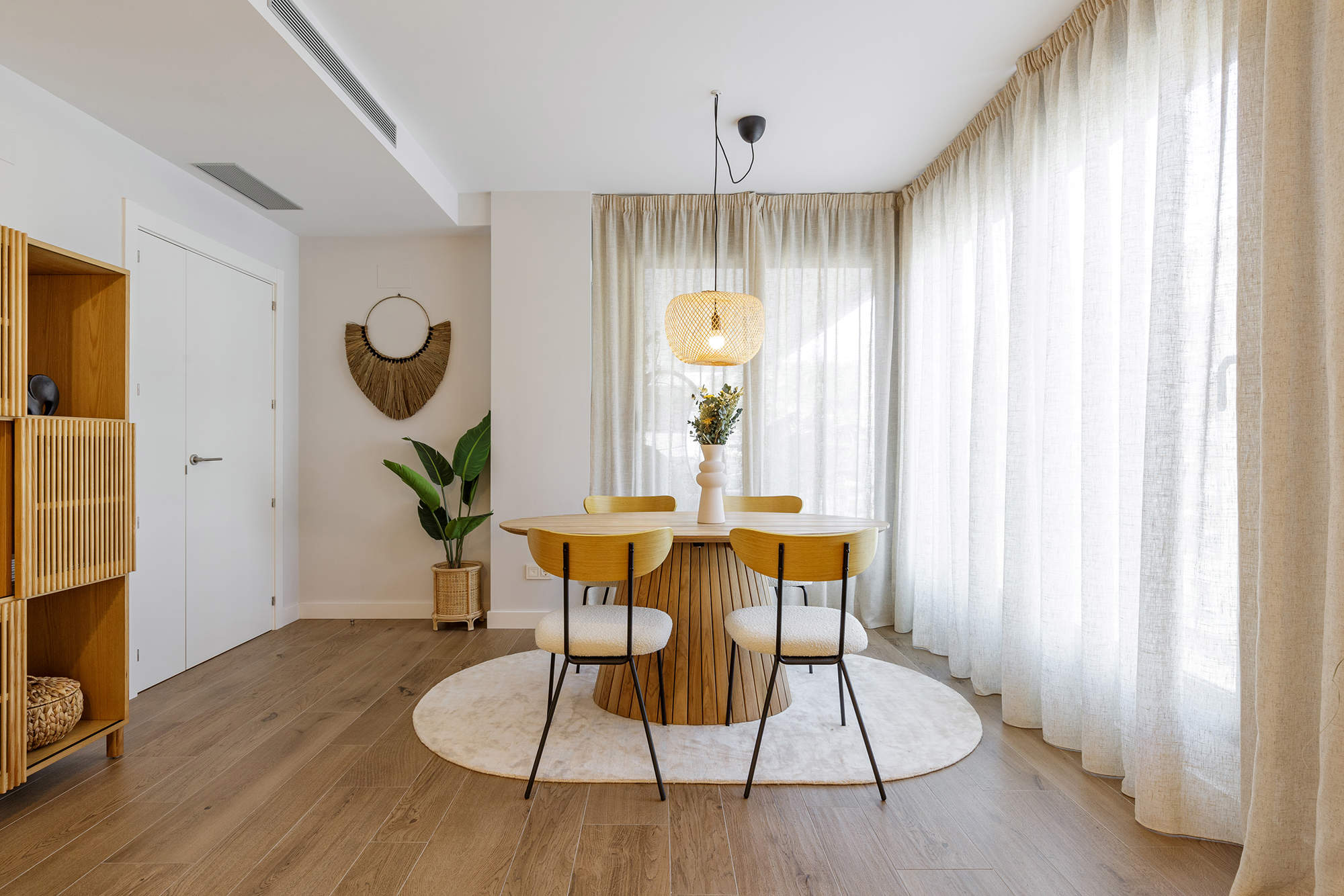 Comedor con mesa de madera redonda, sillas con tapizado bouclé y lámpara de fibras