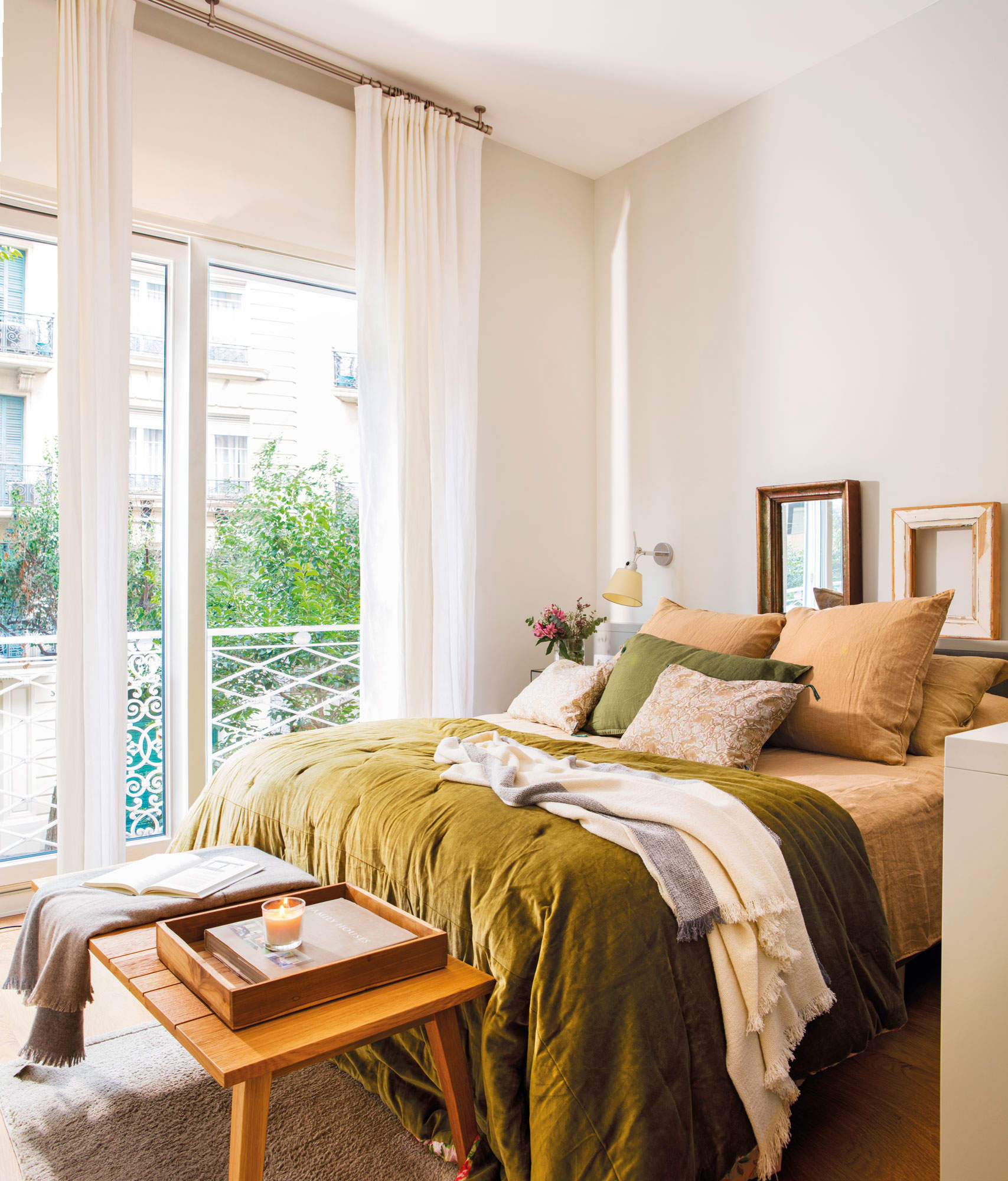 Dormitorio en tonos verdes y mostazas, con gran edredón, plaid y mantita sobre un banquito.