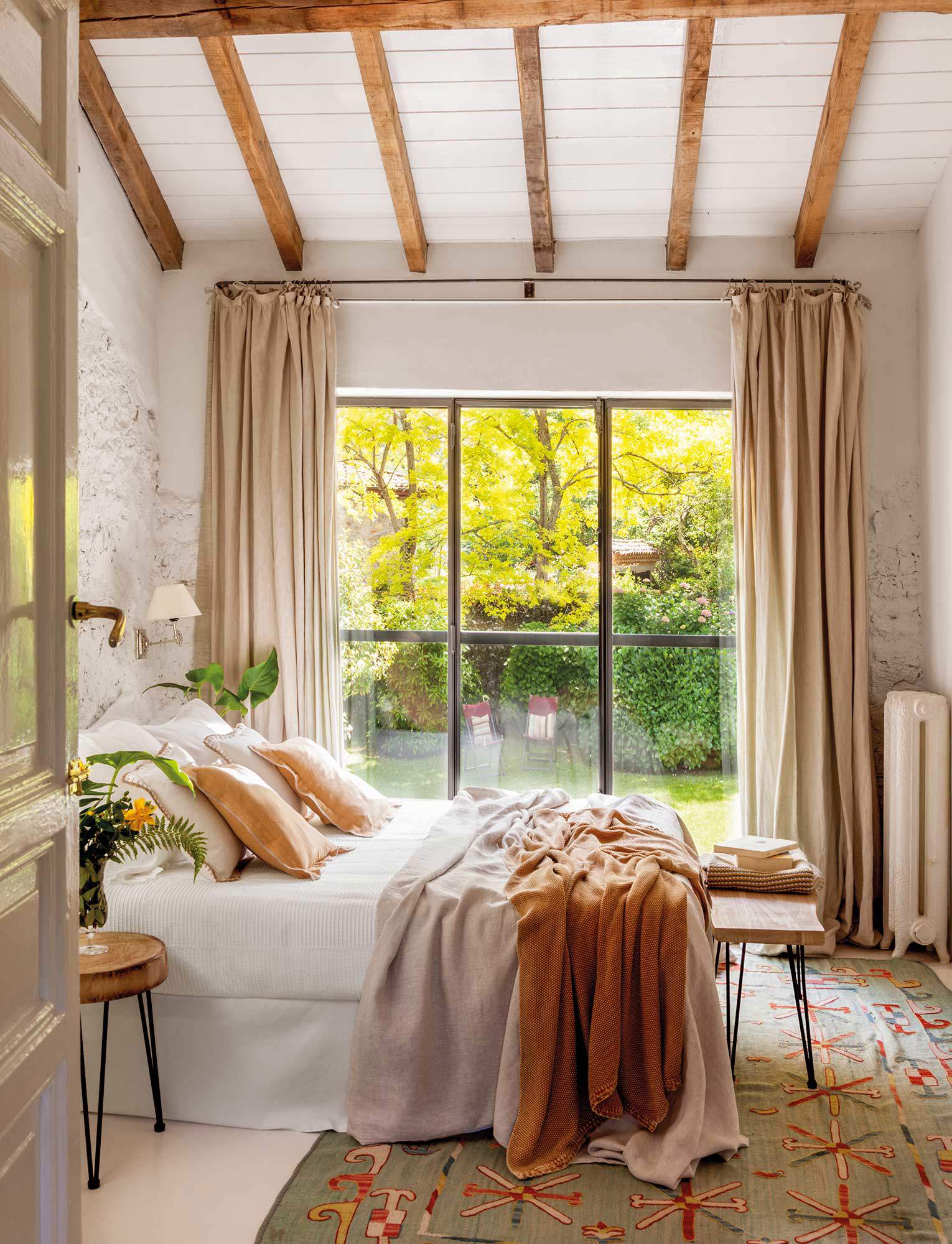Dormitorio con vigas de madera, tonos neutros y gran alfombra en color aguamarina