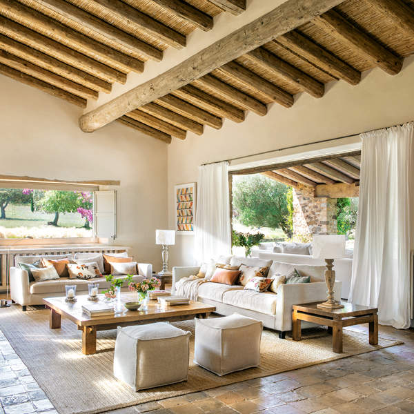 Salón rústico y cálido con sofá blanco con pavimento de piedra y techo de vigas de madera