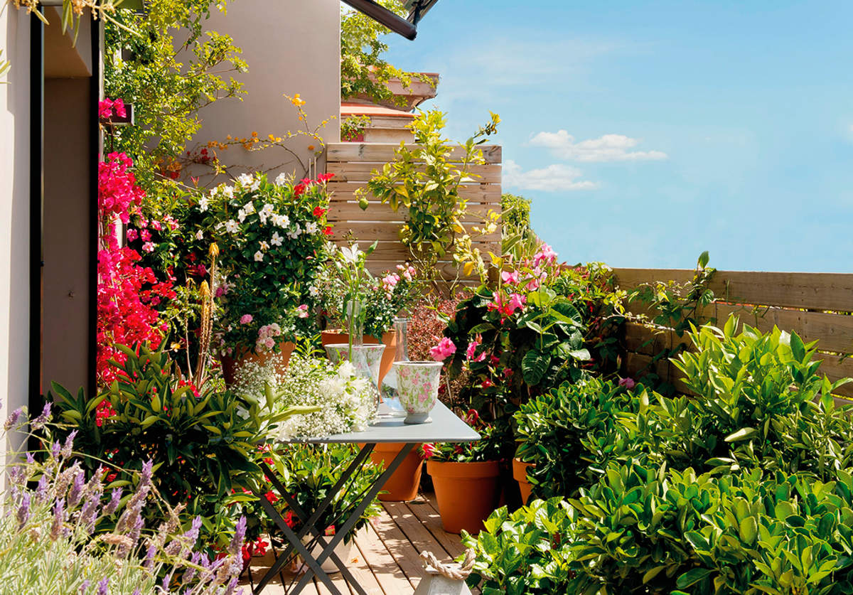 Terraza pequeña con mesa plegable de jardín de metal, macetas con plantas y farol con vela