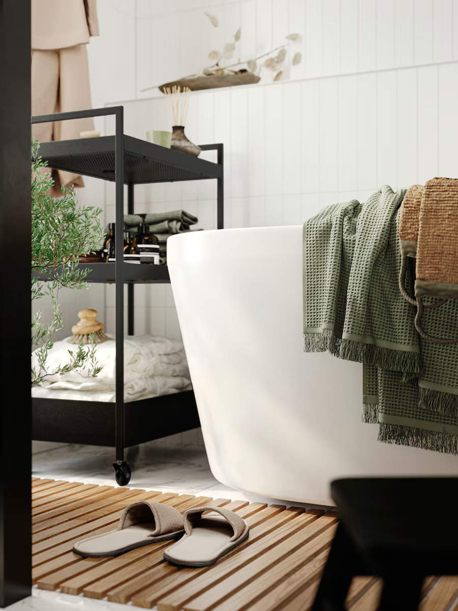 Un baño con bañera exenta, materiales naturales y carrito negro de almacenaje