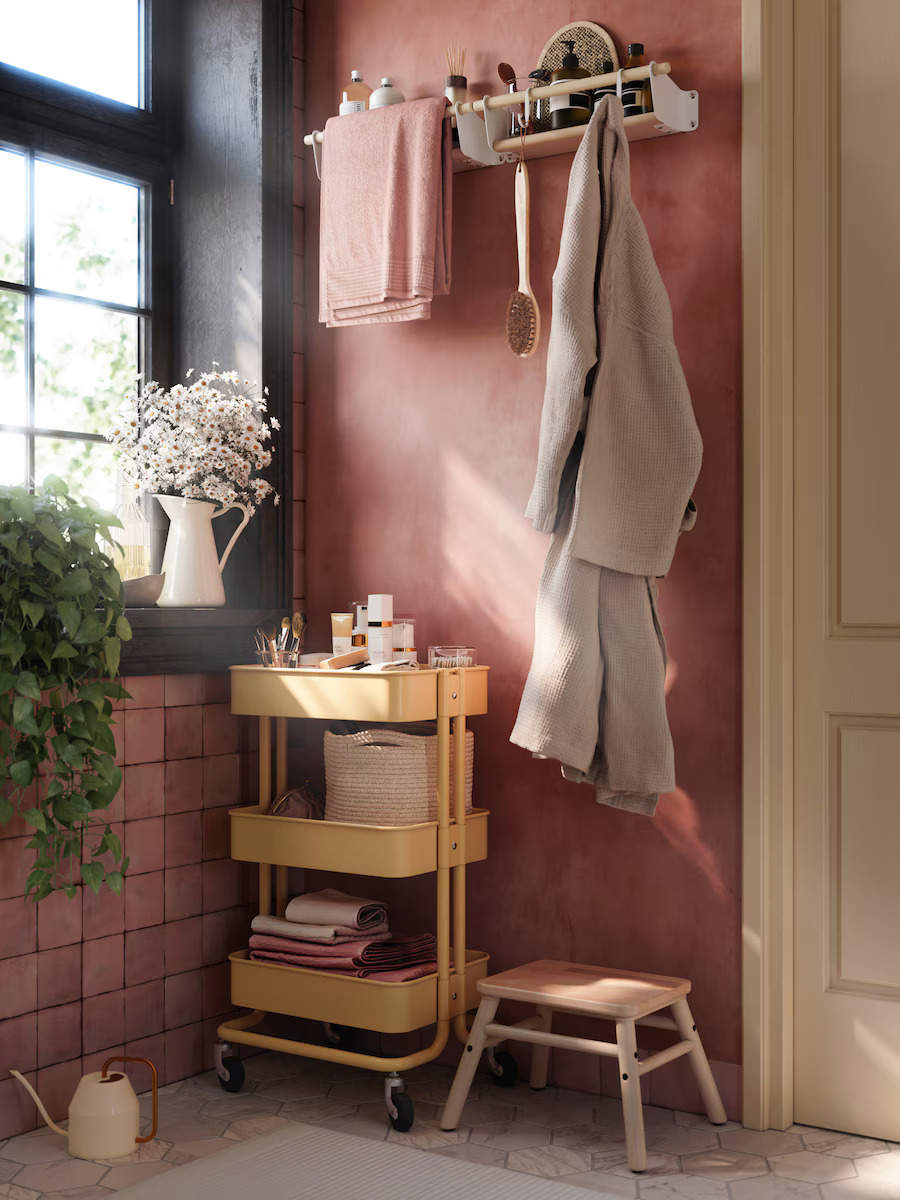 Baño de color rosa con carrito de almacenaje y estante de pared