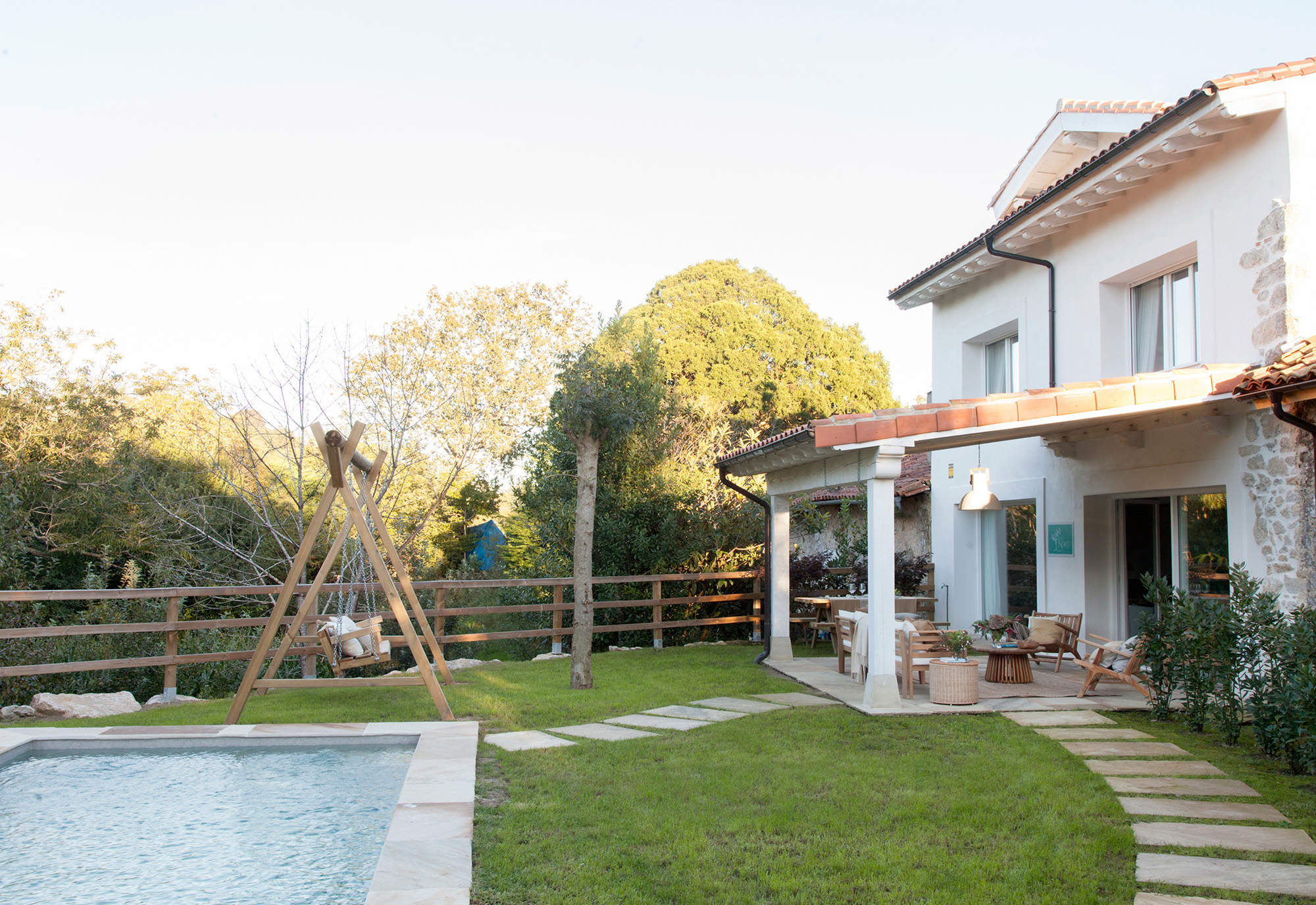 Jardín con camino de baldosas entre la casa y la piscina