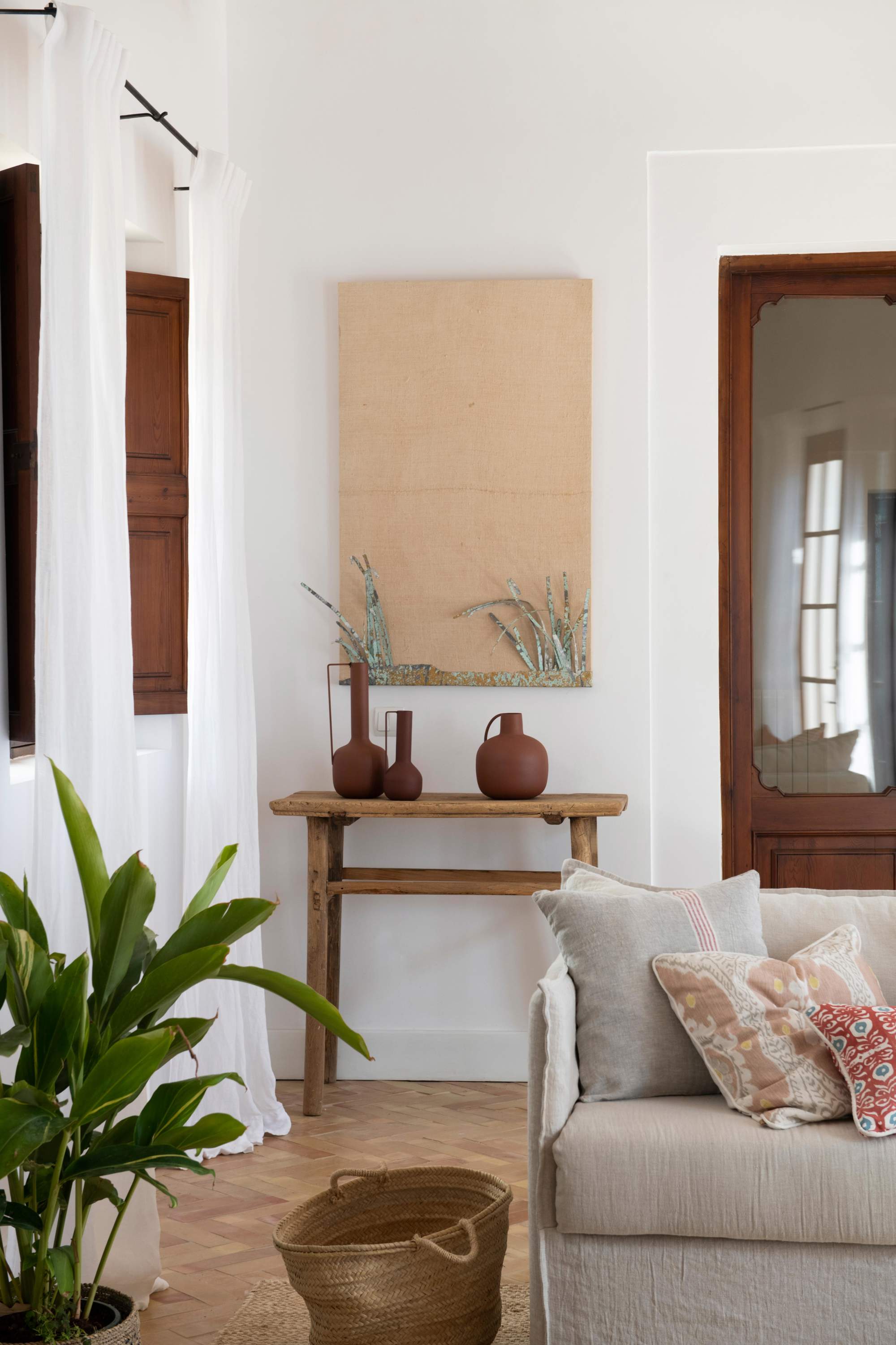 Salón con consola de madera detrás del sofá, cesta, cuadro y jarrones de cerámica