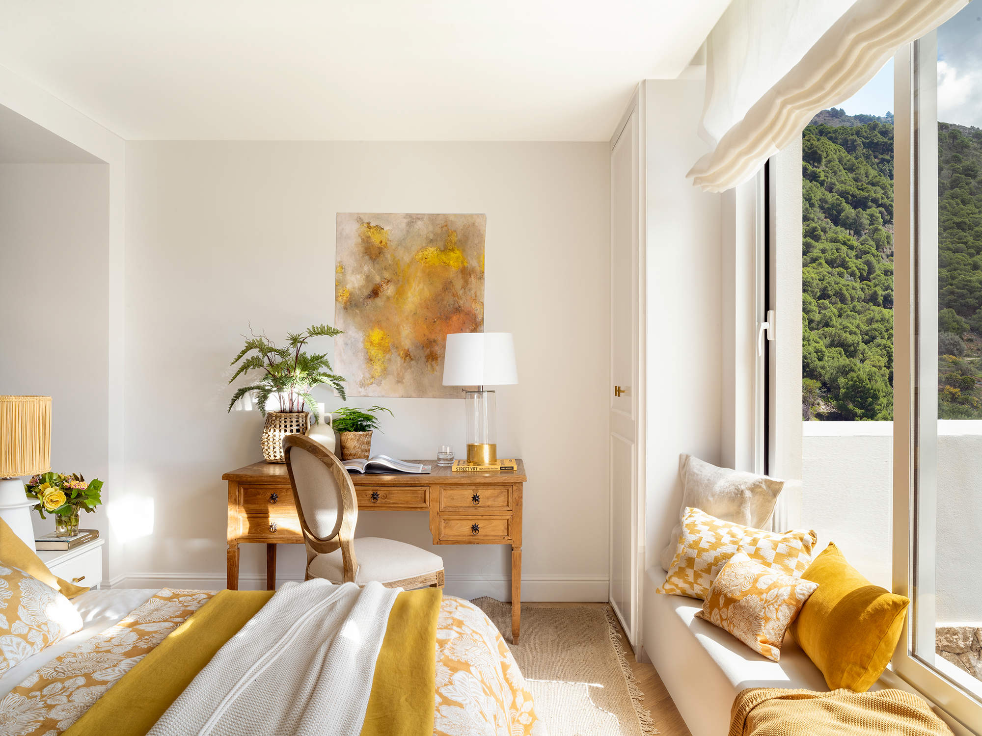Dormitorio de verano en colores ocres con escritorio de madera, silla con respaldo de medallón y cuadro en colores mostaza.