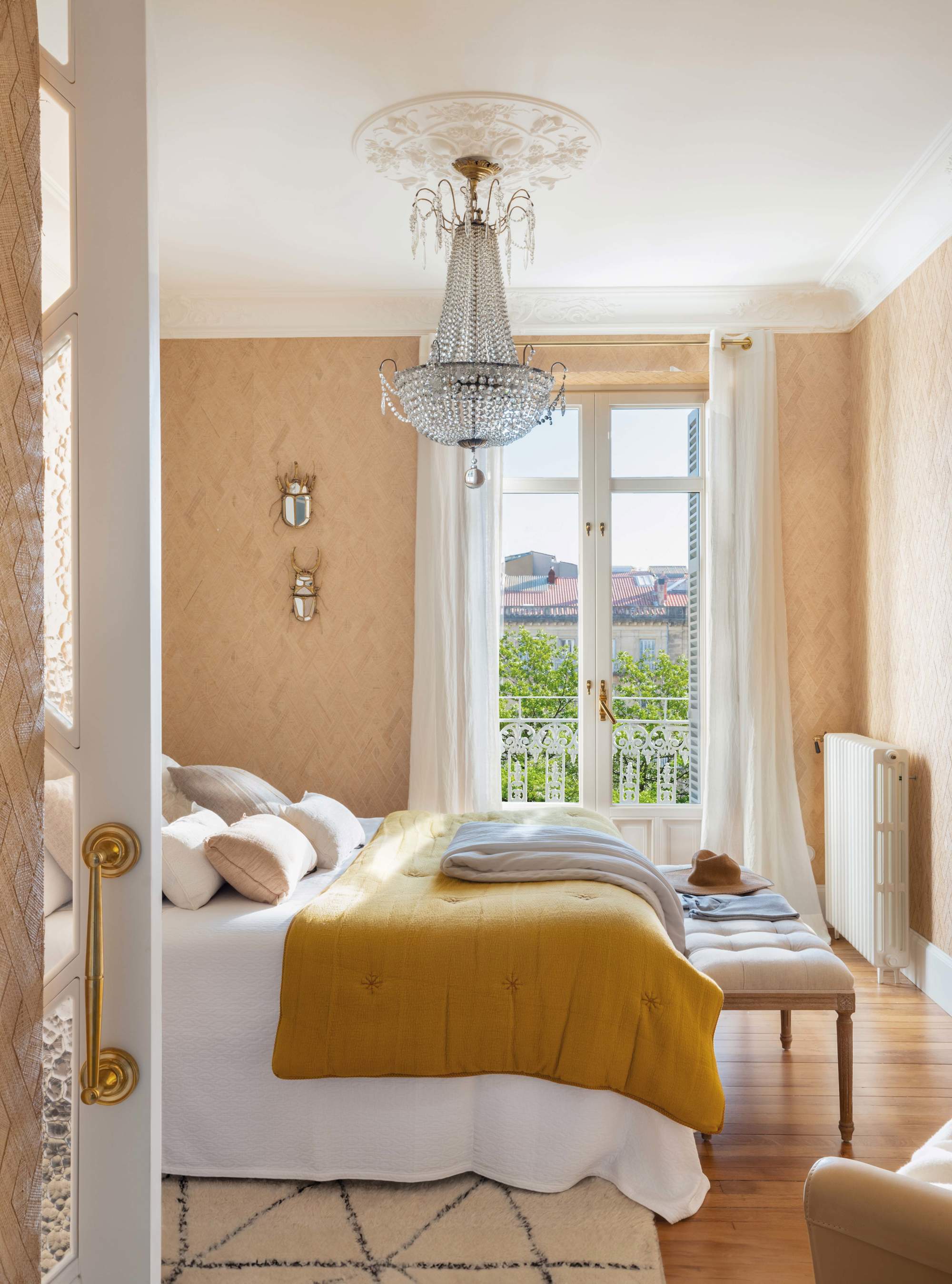 Dormitorio con lámpara chandelier en rosetón y papel pintado color beige y estampado
