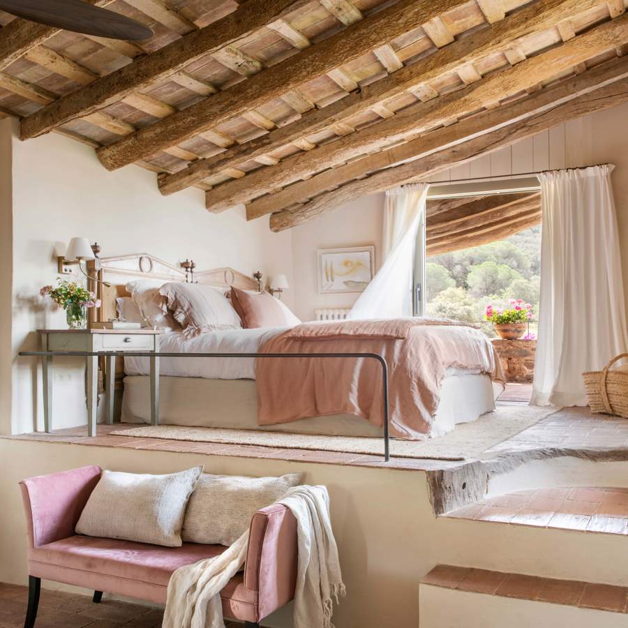 Dormitorio abuhardillado en dos niveles con cama, vigas y sofá rosa
