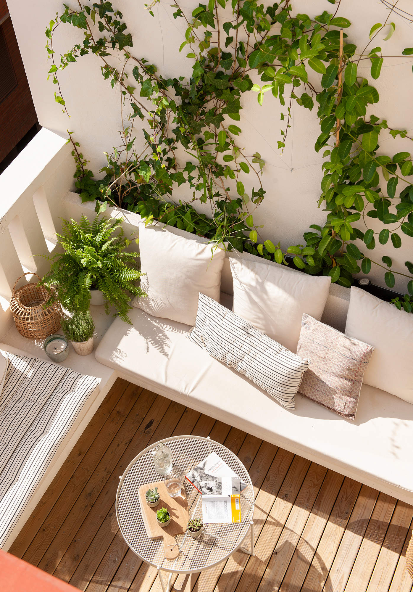 Terraza pequeña con banco en forma de L y muro decorado con plantas.