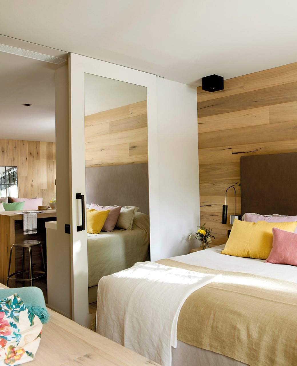 Dormitorio con pared forrada de madera y puerta corredera con espejo.