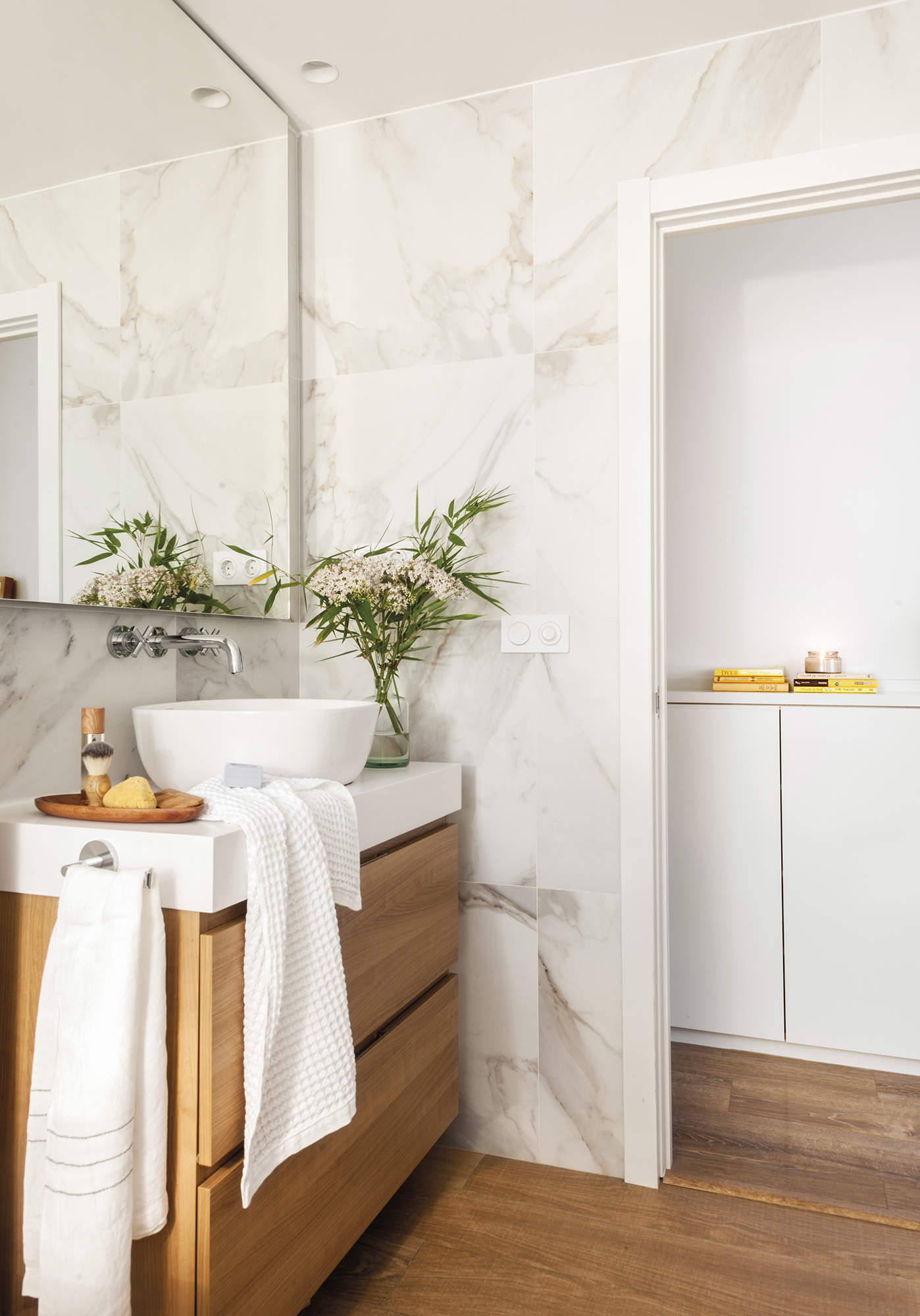 Cuarto de baño con mueble de lavabo de madera y espejo hasta el techo.