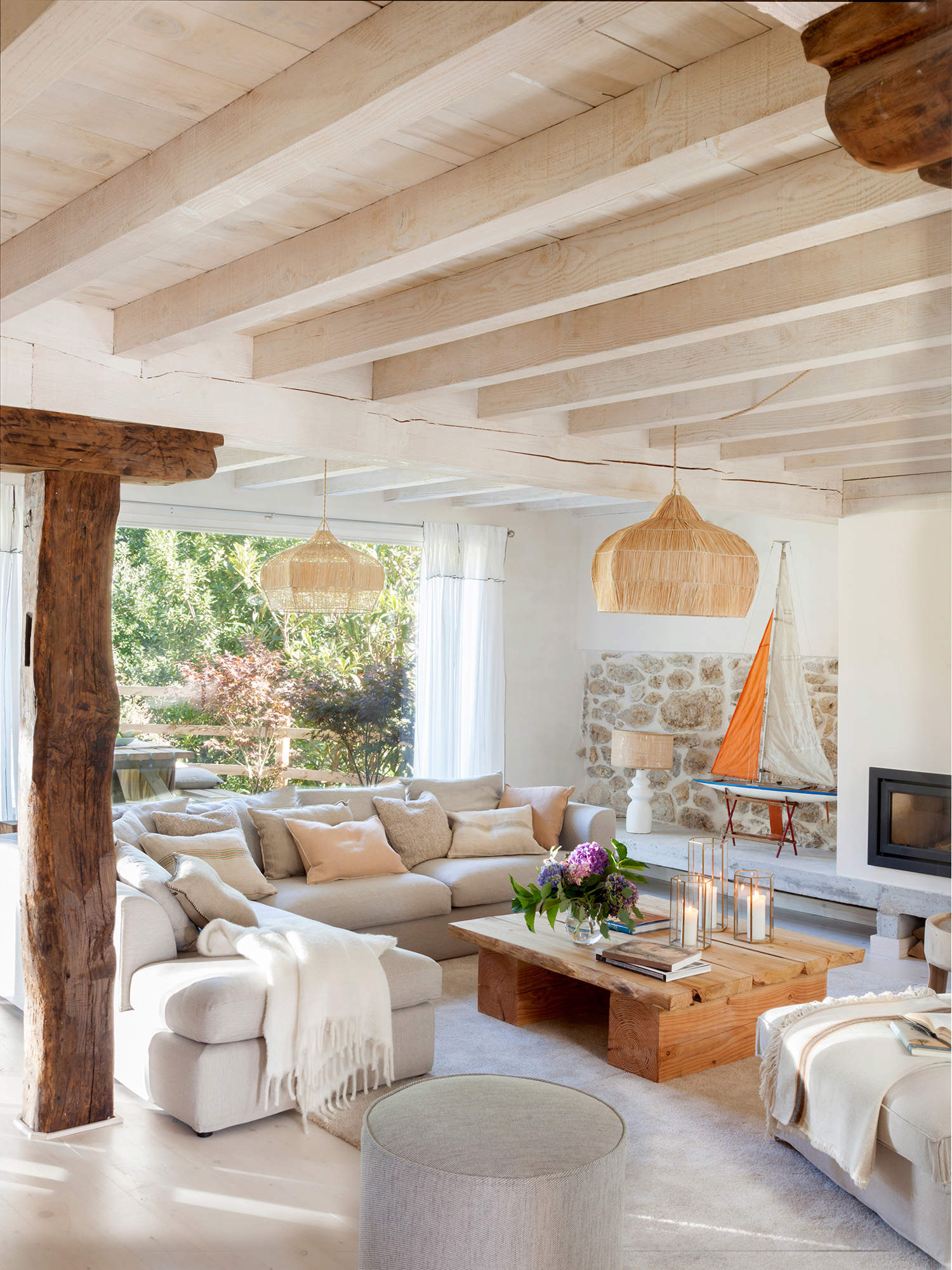 Salón de verano con techo de vigas, sofña con chaise longue y mesa de madera.