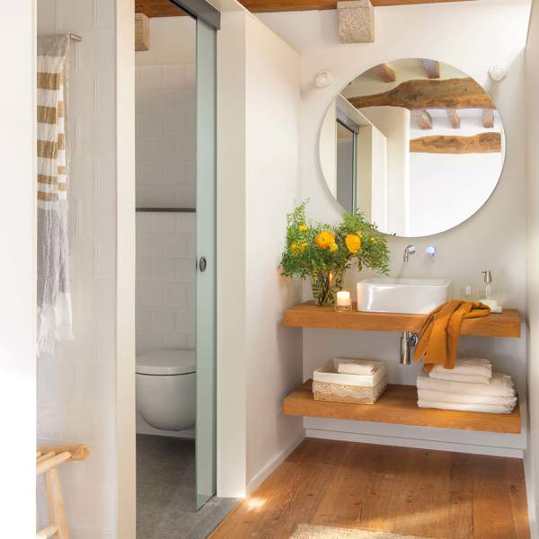 Baño pequeño con vigas de madera, mueble volado y espejo redondo