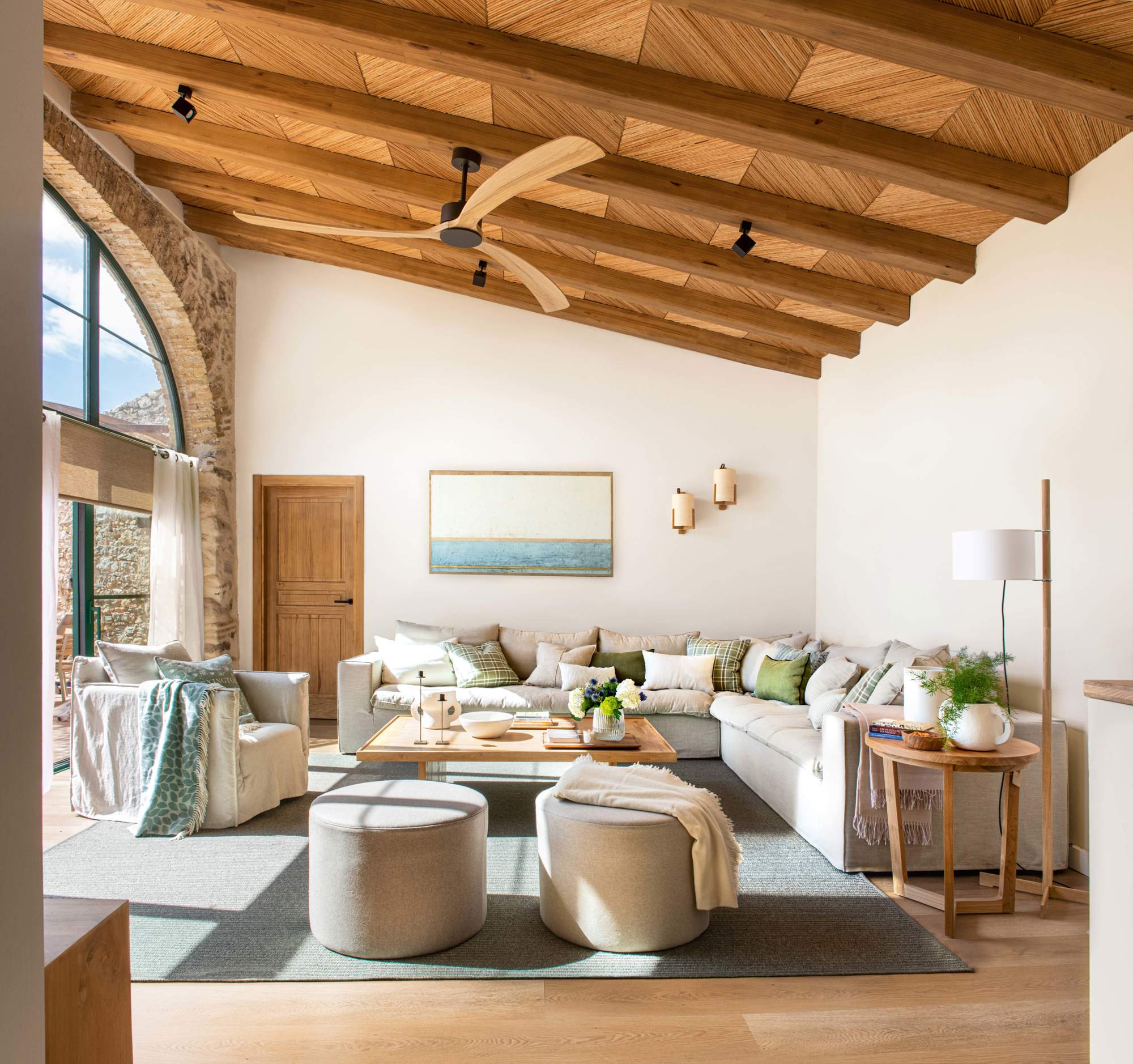 Salón con techo de madera, sofá rinconera, pufs y butacas.