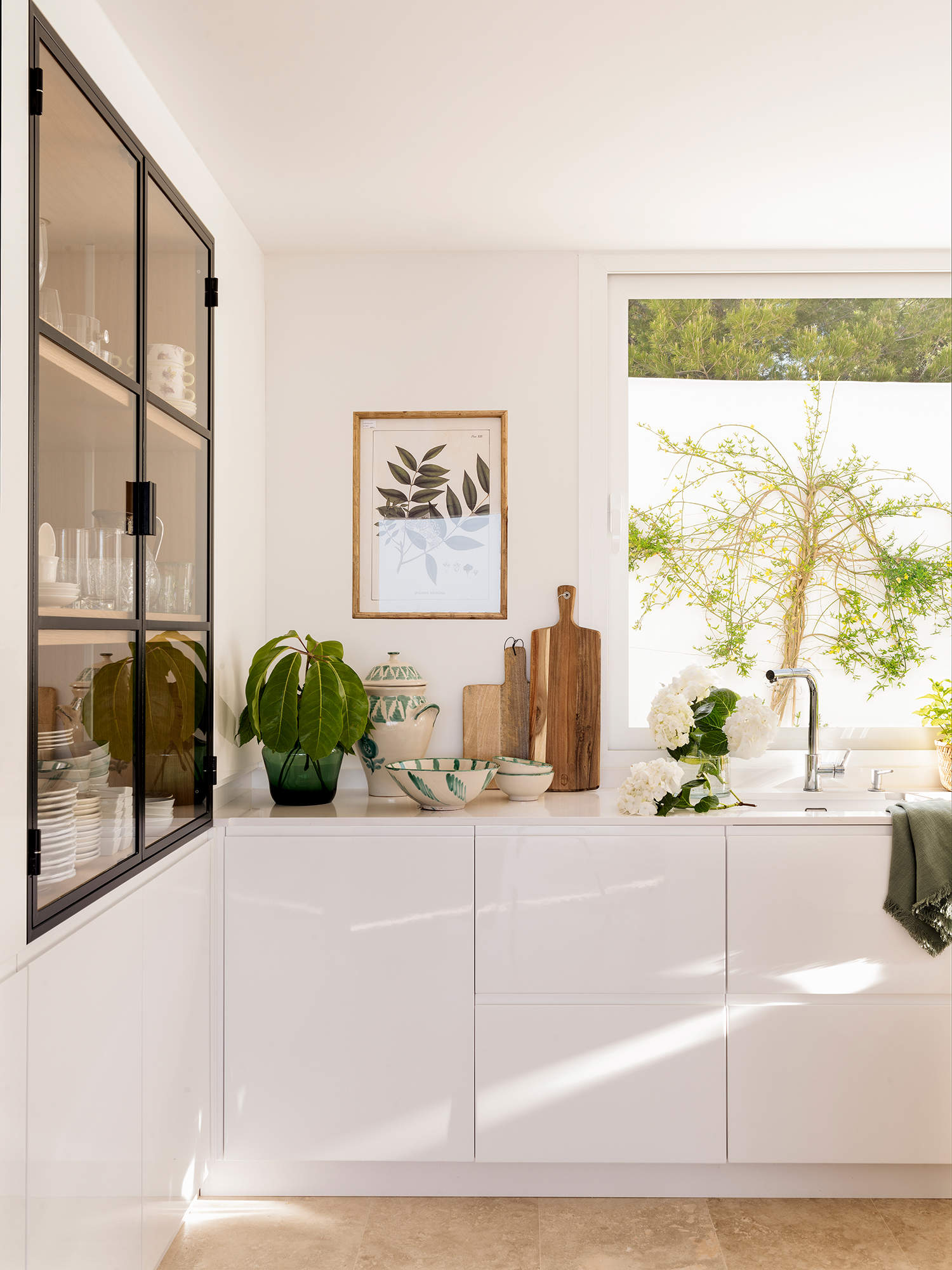 Cocina en forma de L, con armarios blancos en un frente y una gran vitrina en otro. 