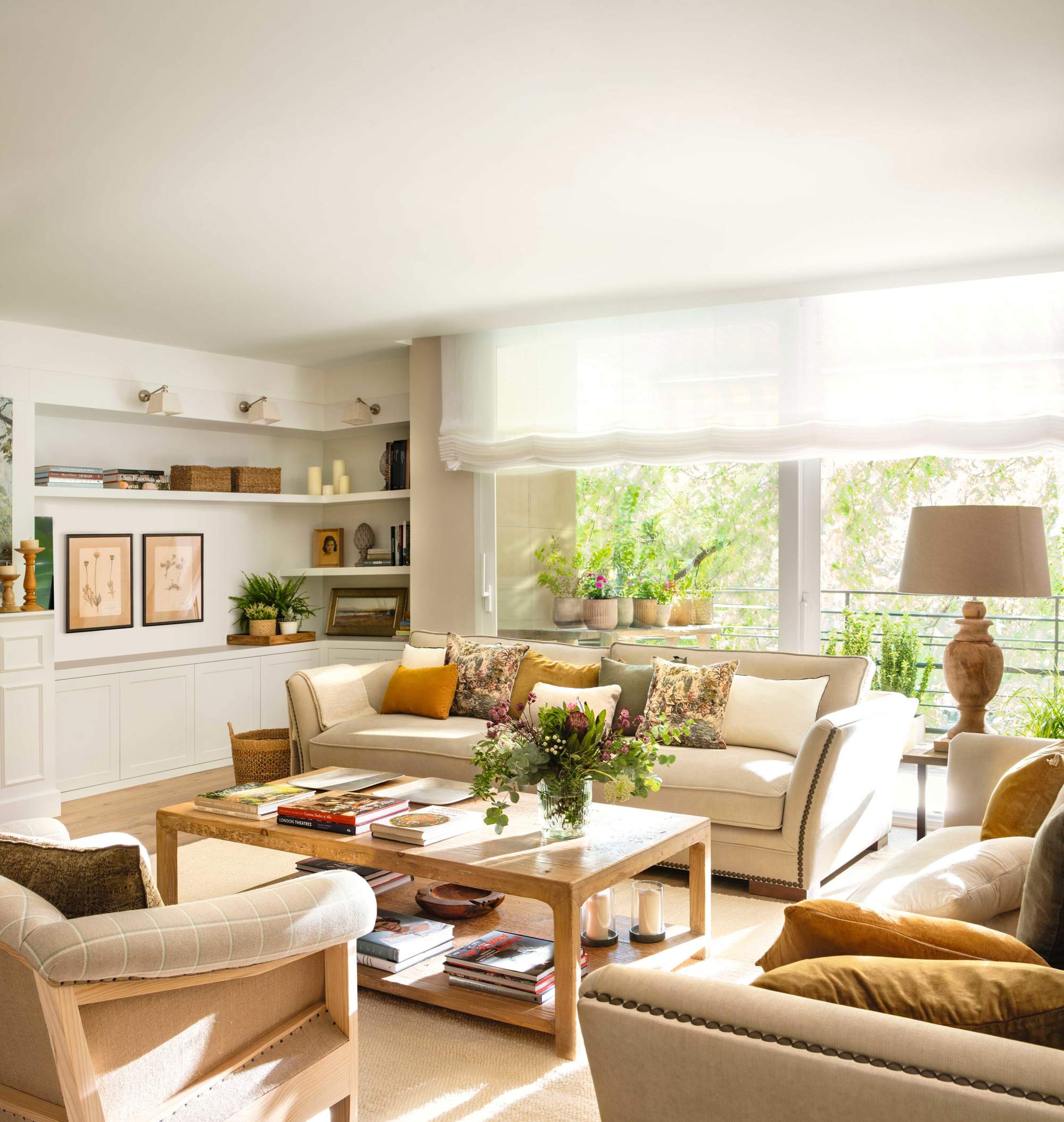 Salón con sofás en L, sillones tapizados de cuadros, mesa de madera y mueble librería