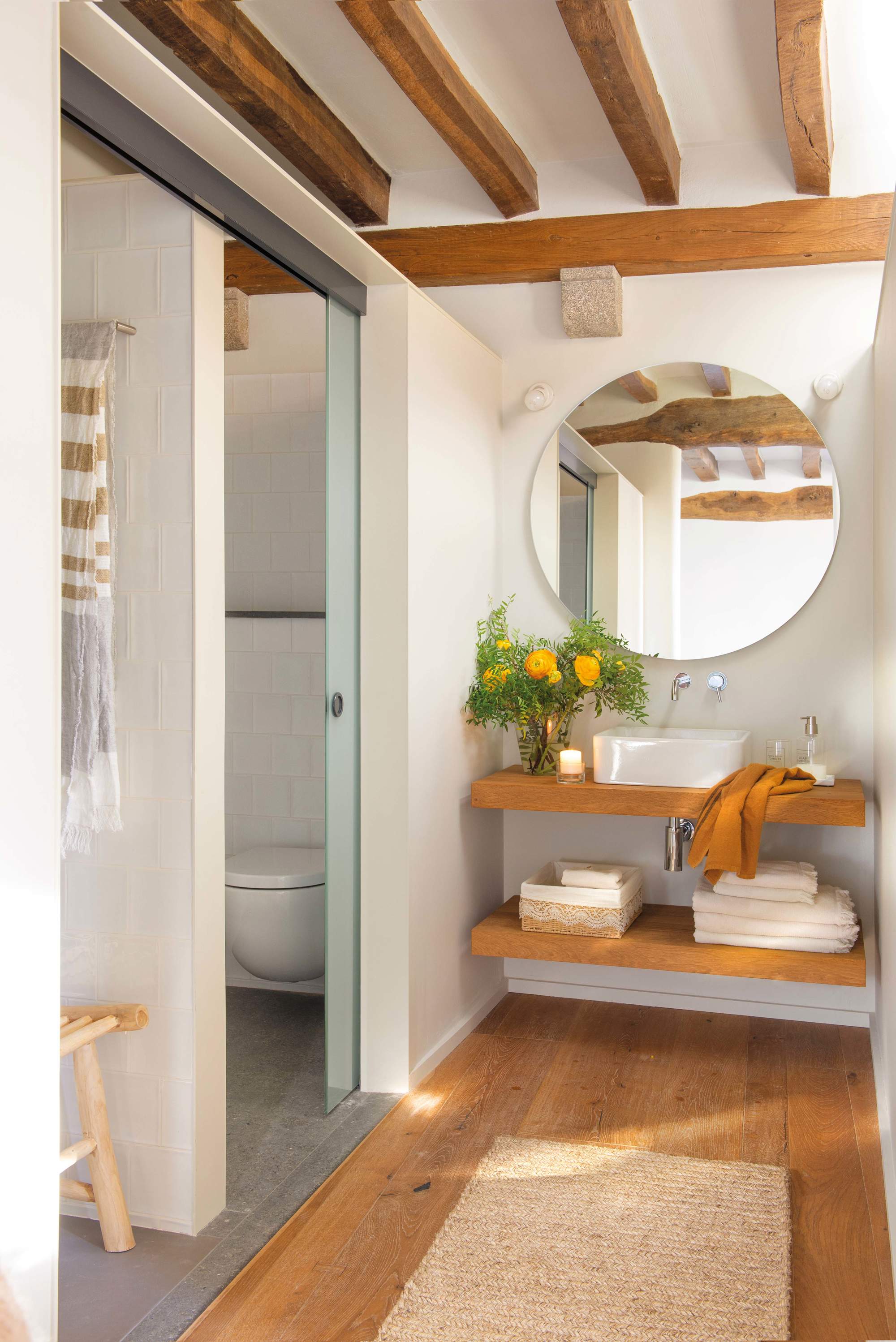 Baño pequeño con vigas de madera, mueble volado y espejo redondo