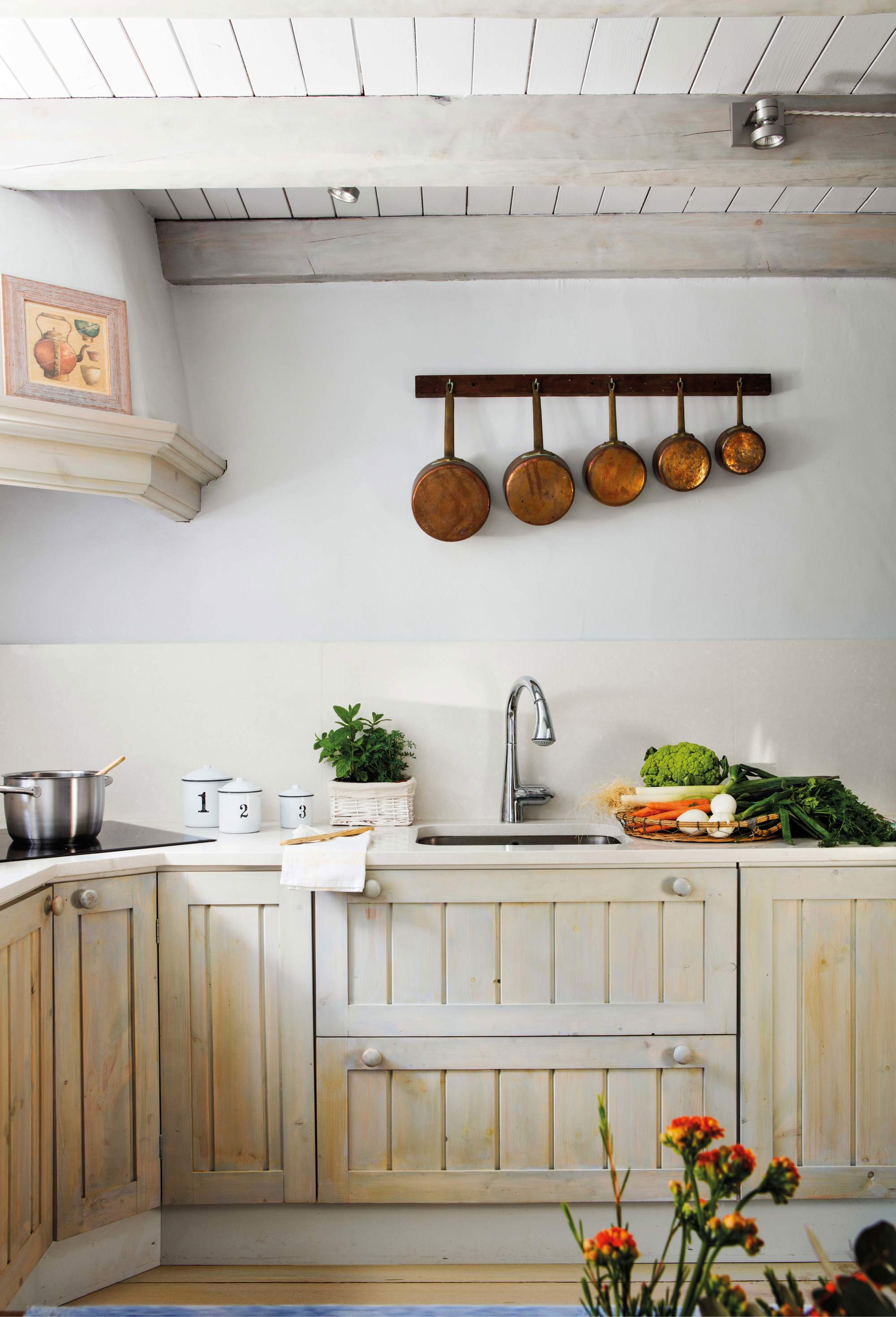 Cocina de madera blanca alistonada con cazos de cobre colgados