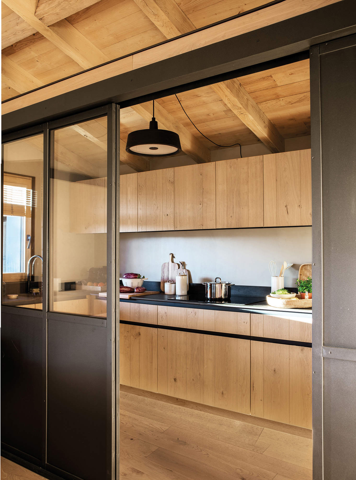 Cocina con muebles en madera y falsa pared de cristal de entrada 