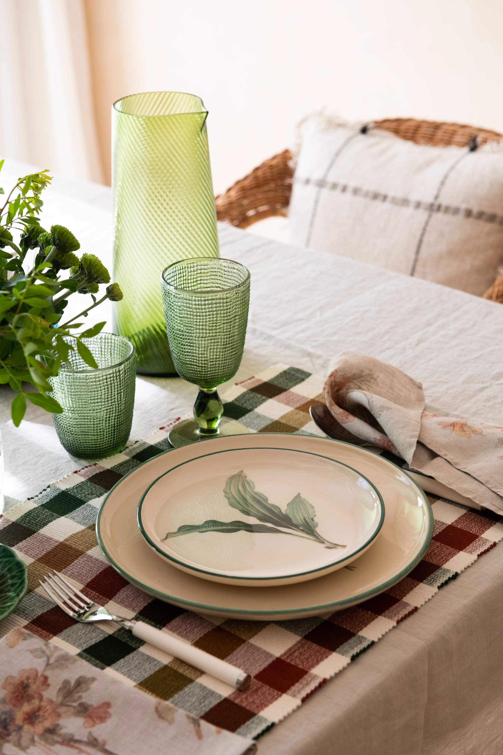 Mesa de comedor con mantel individual de cuadros, plato estampado y copas verdes