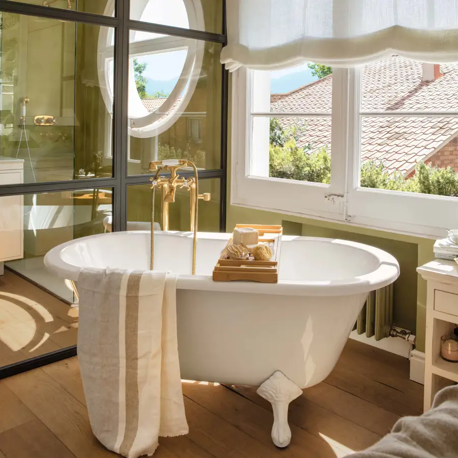 Bañera exenta con grifería vintage dorada en baño verde