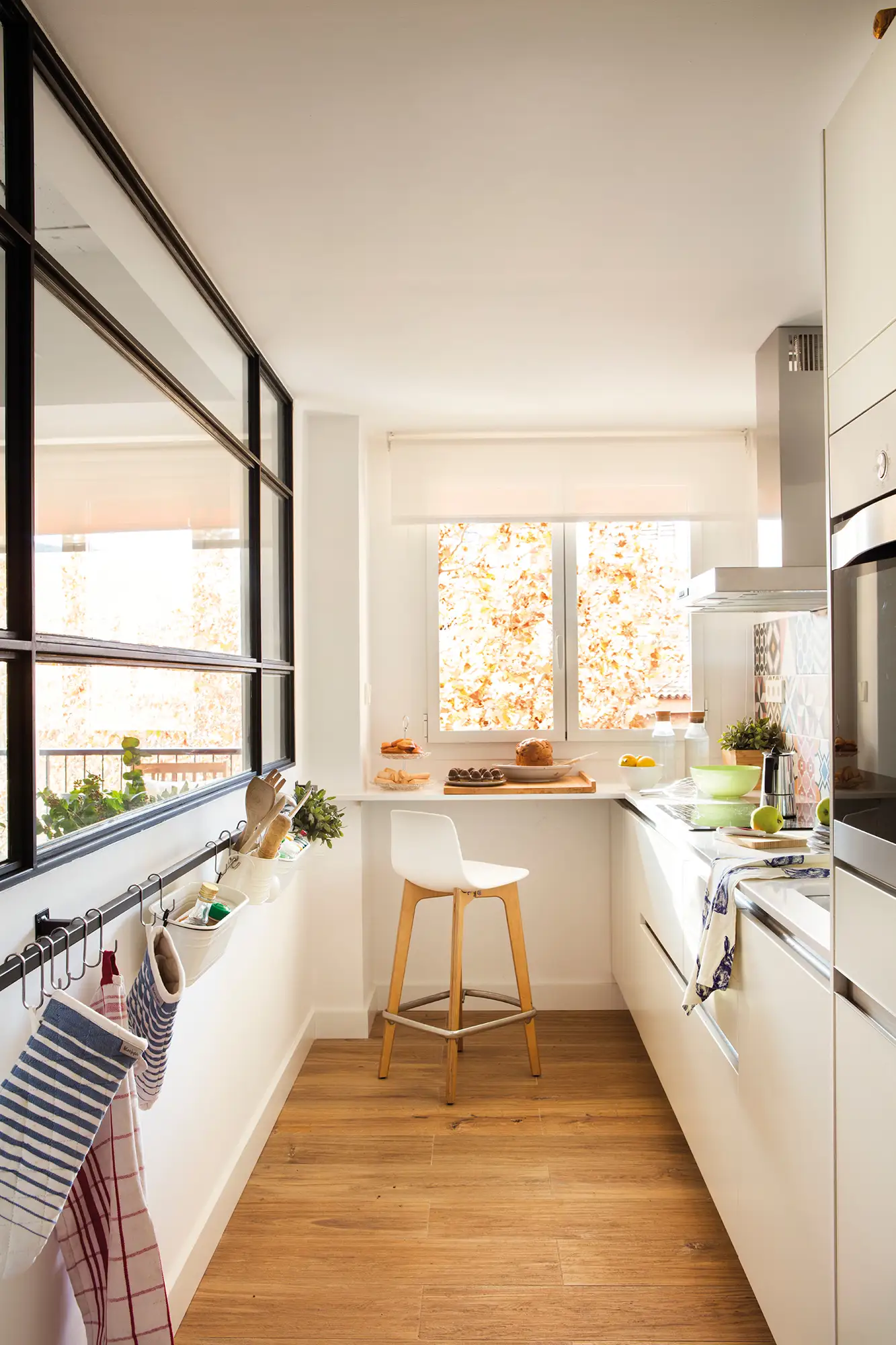 Cocina pequeña en blanco con mini barra de desayunos y gran ventanal al salón.