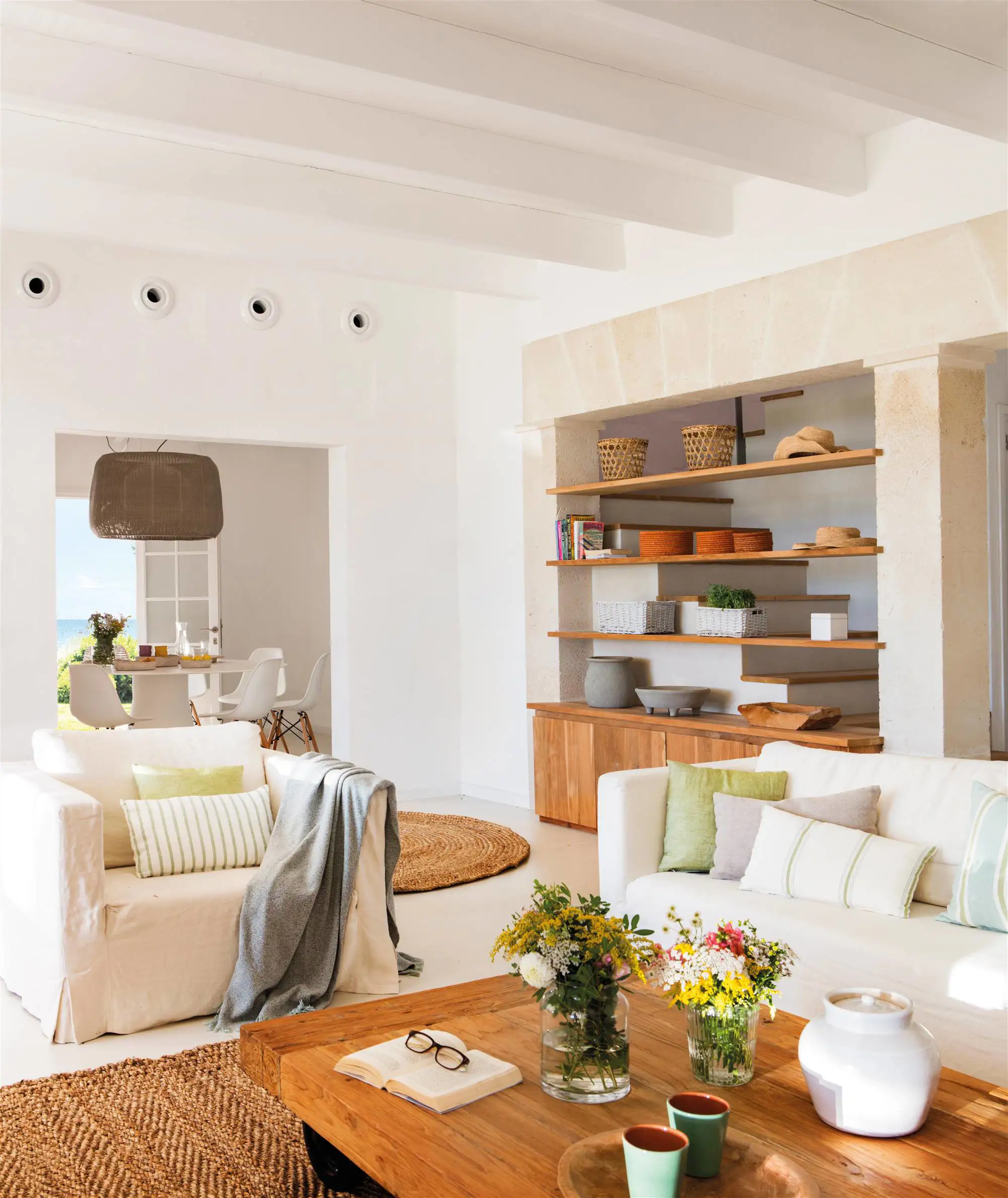 Salón con sofá neutro y mesa de centro con estantería de madera y comedor al fondo