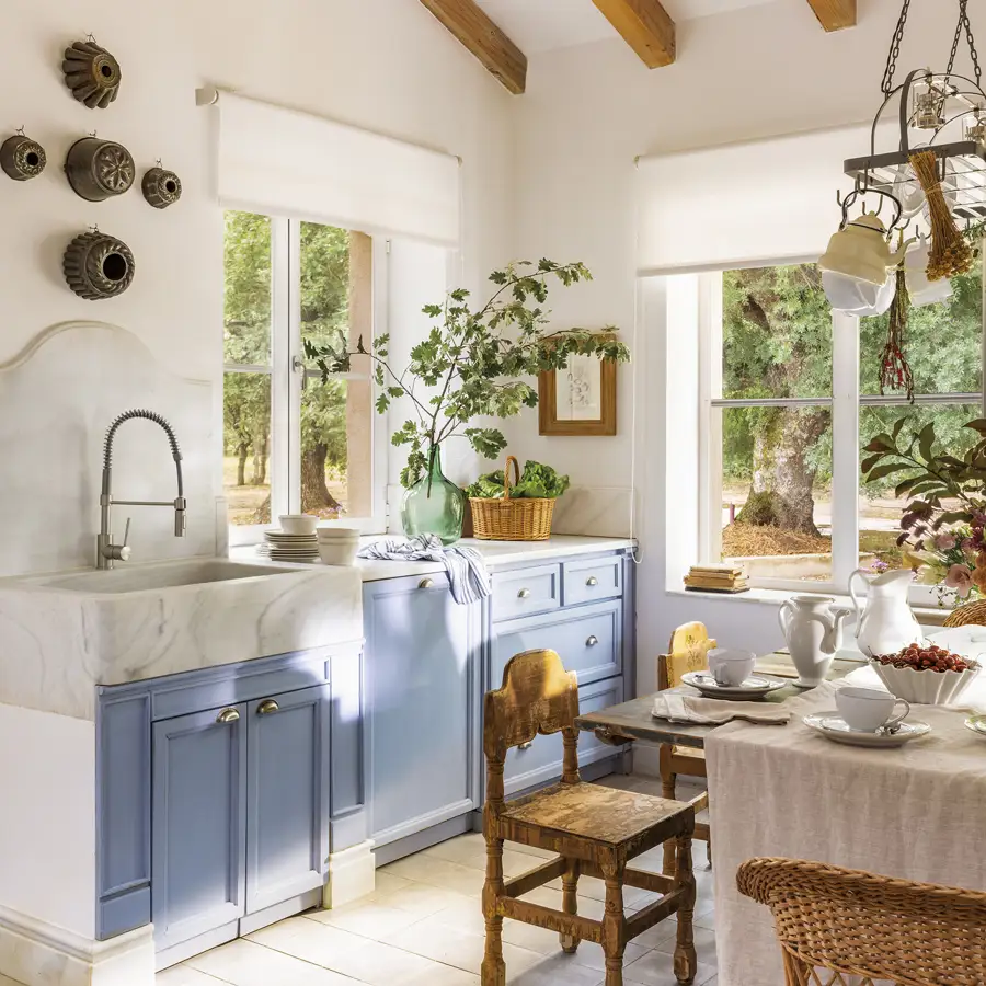 Cocina campestre con muebles azules, mármol blanco y vigas de madera