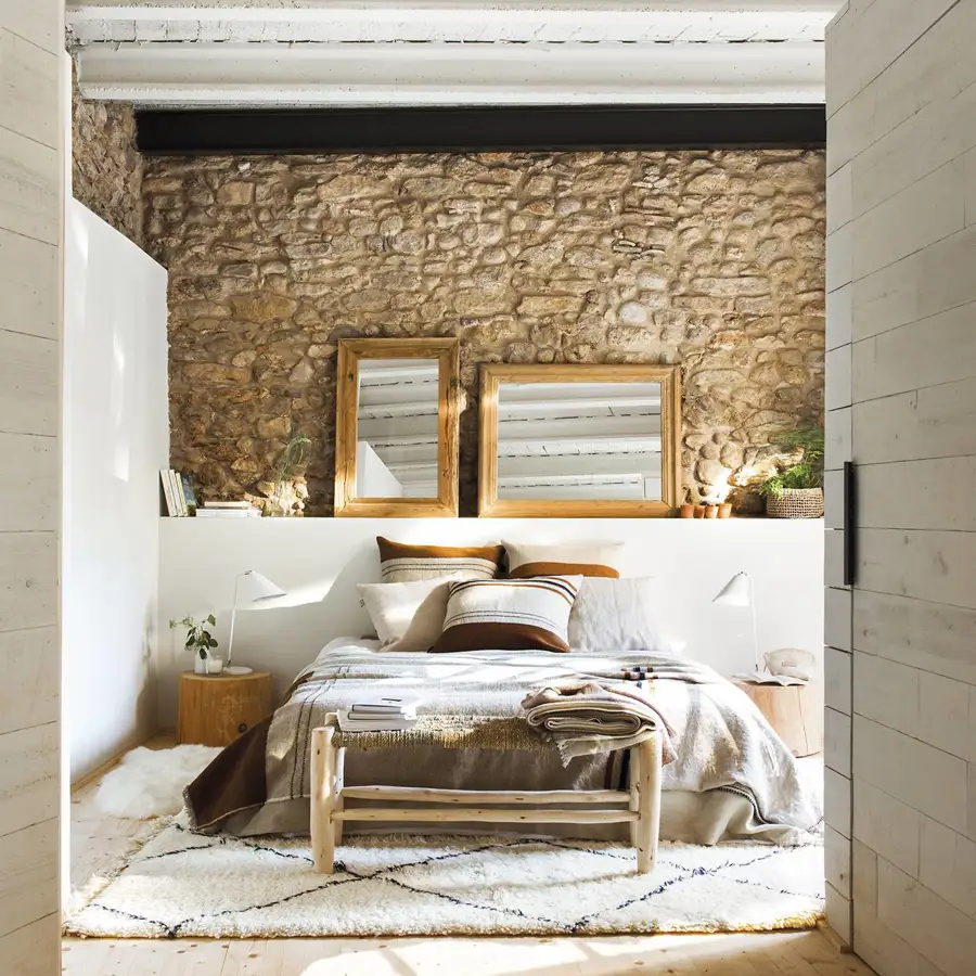 Dormitorio rústico con vigas de madera blancas y pared de piedra