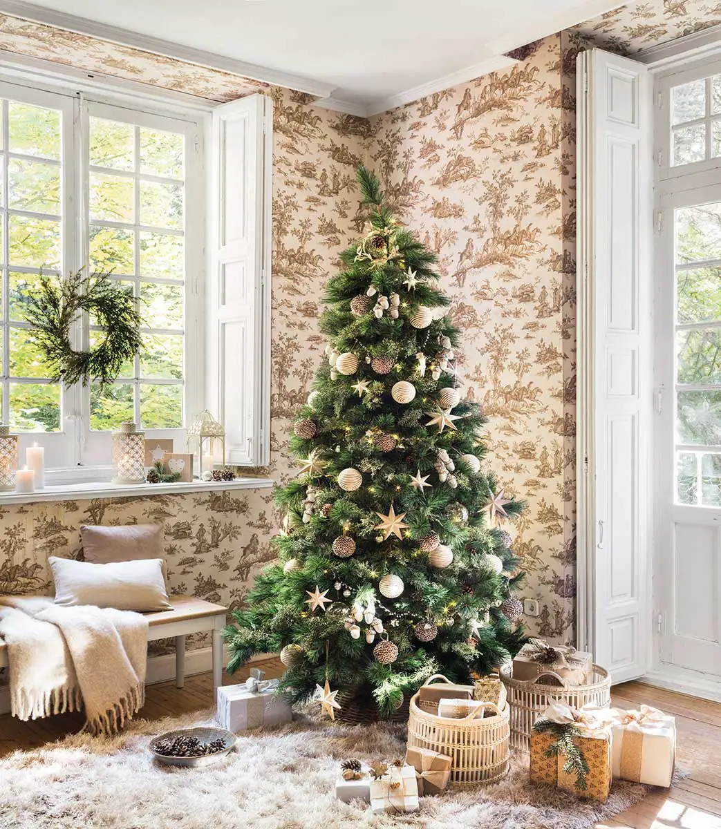 Árbol de Navidad con adornos grandes, pocos y pared con papel pintado beige.