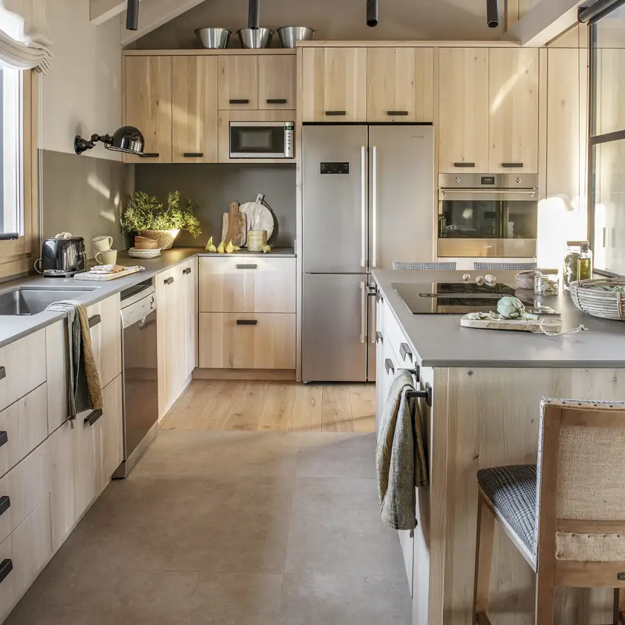 cocina con isla con muebles de madera y electrodomésticos en acero, encimera de piedra gris, suelo de gres y parquet, fregadero, plantas