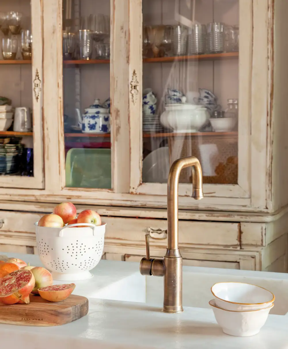 Detalle de grifería dorada en cocina con vitrina al fondo