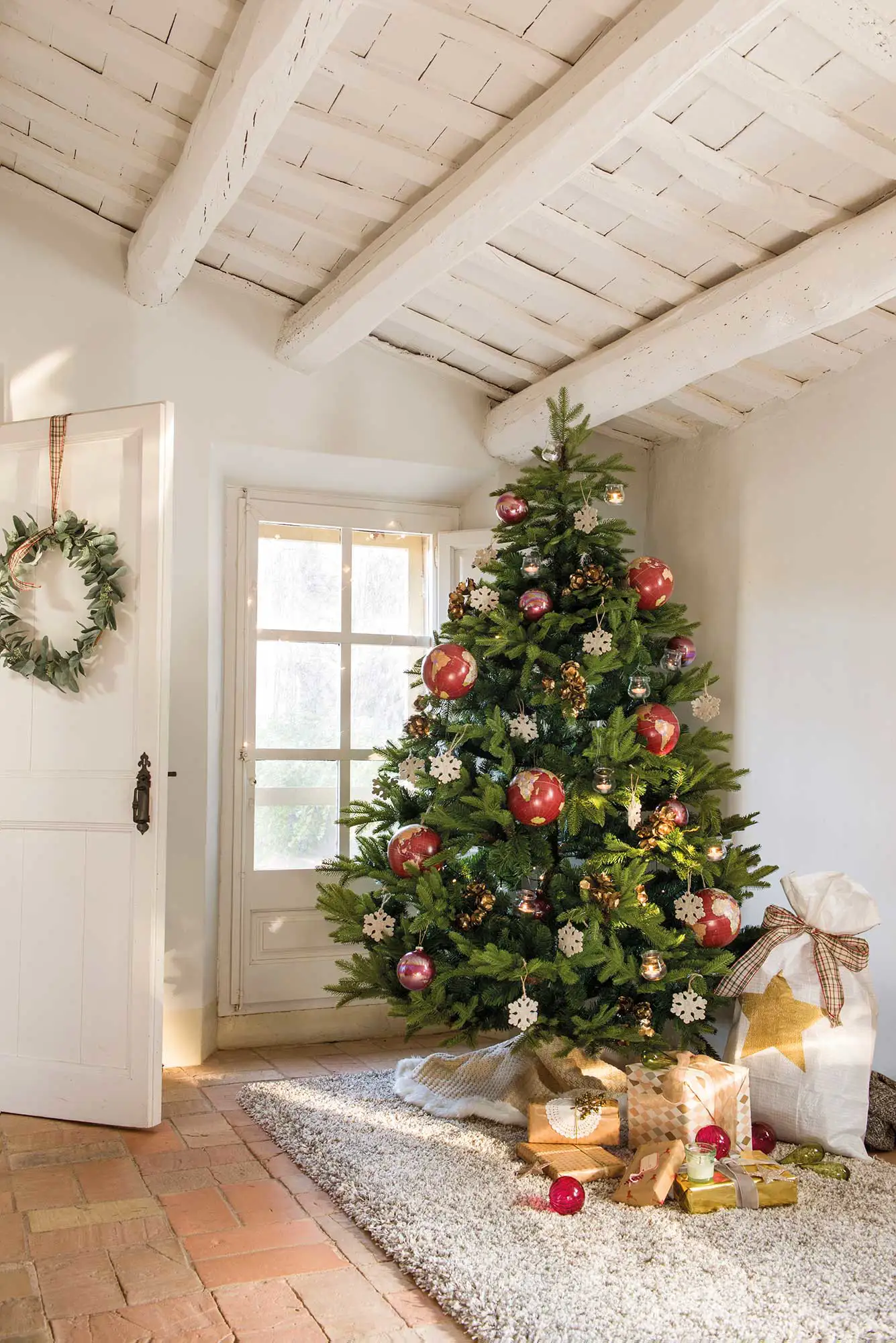 Árbol de navidad grande con adornos en la entrada de casa. Alfombra en el suelo.