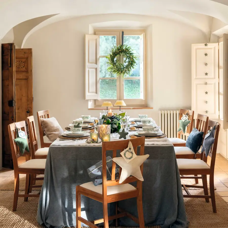 Comedor de Navidad con mesa vestida, corona en ventana y silla decorada