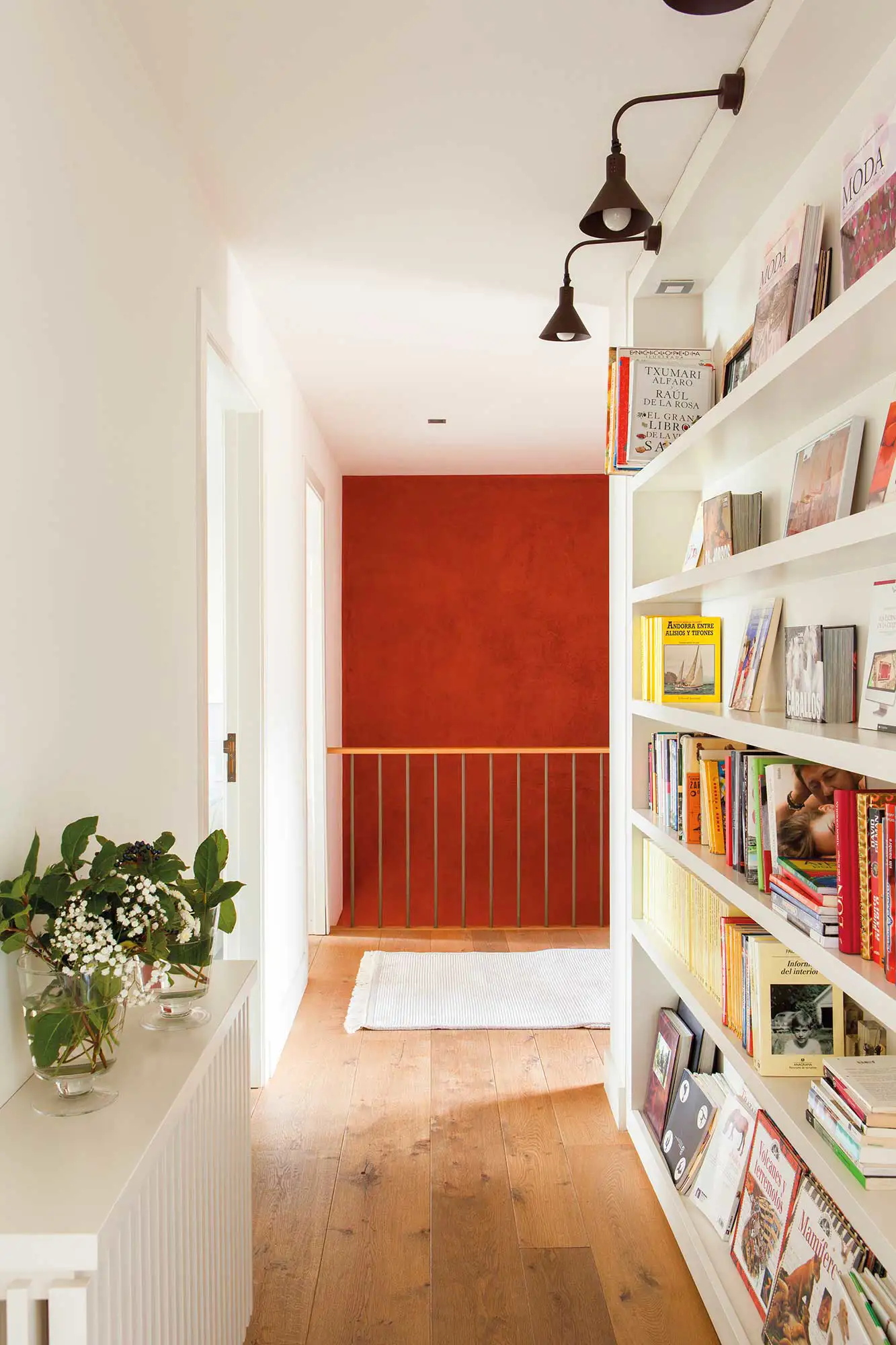 Pasillo con librería de obra, apliques y pared pintada en tonos rojizos