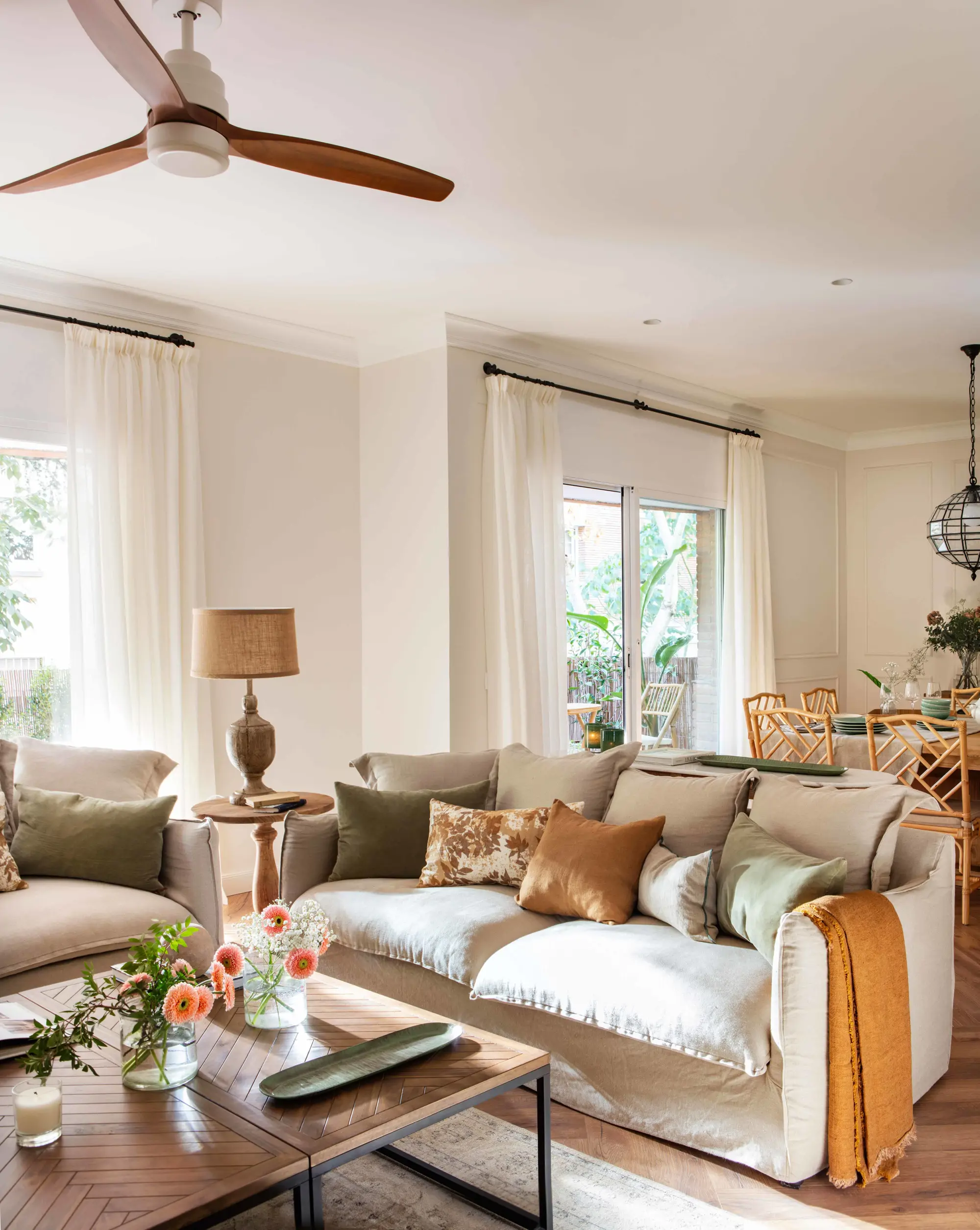 Salón con sofá neutro, ventilados y comedor al fondo