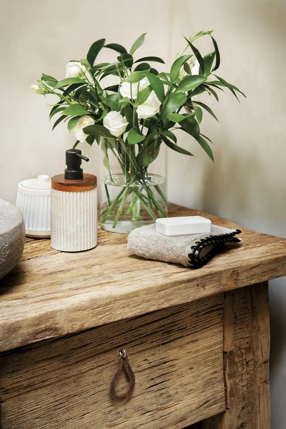 baño, mueble de madera con cajones, florero, flores blancas, jabón, dispensador de jabón