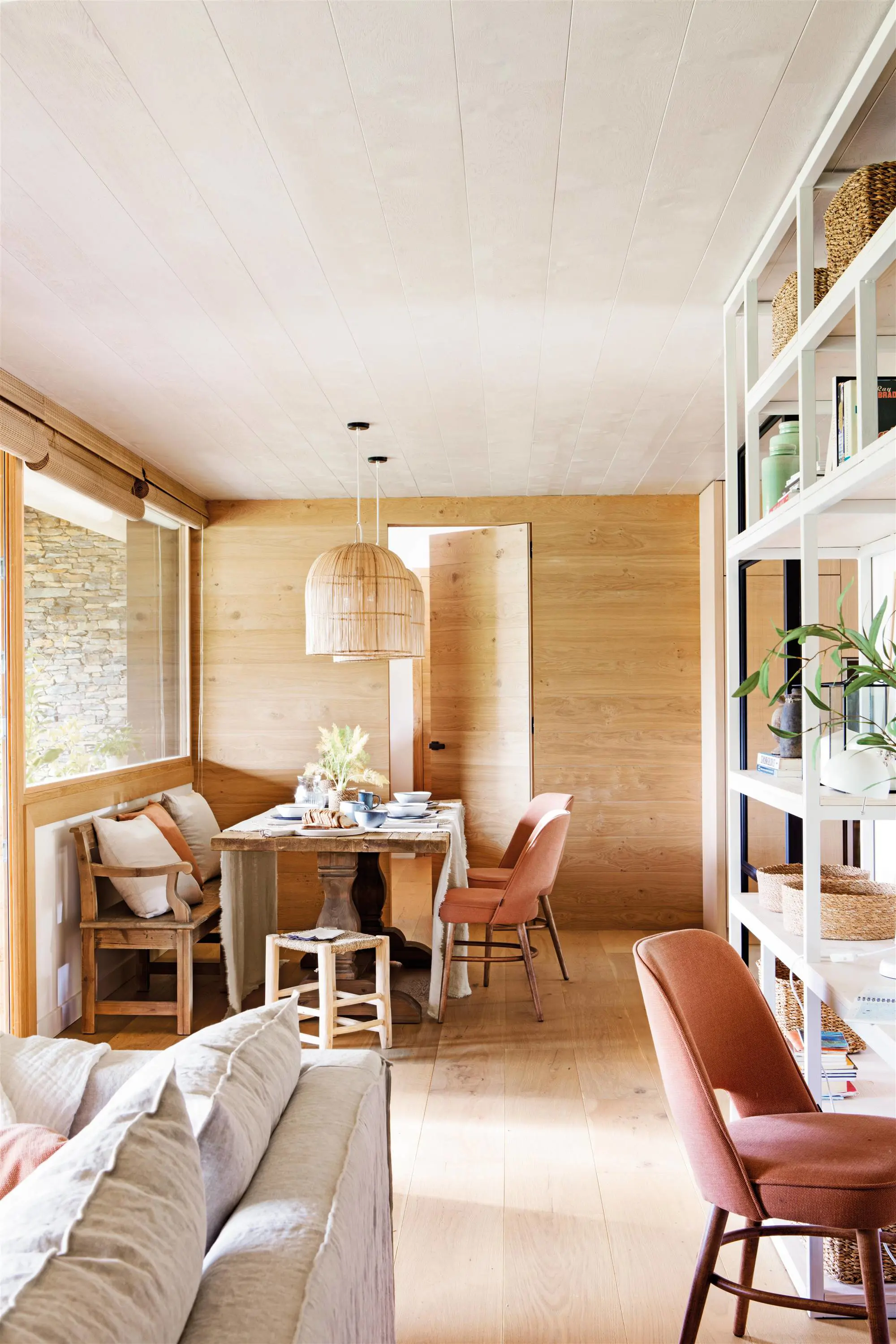 Comedor abierto al salón con pared revestida de madera y puerta invisible