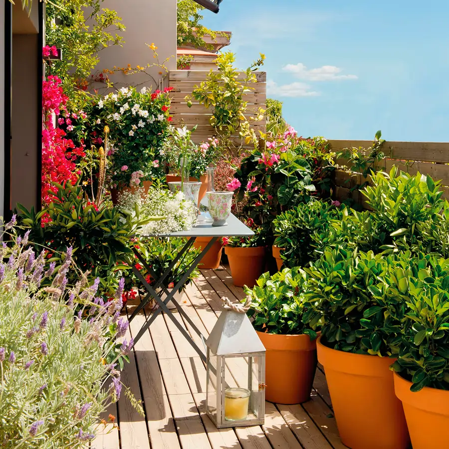 Terraza pequeña con mesa plegable de jardín de metal, macetas con plantas y farol con vela