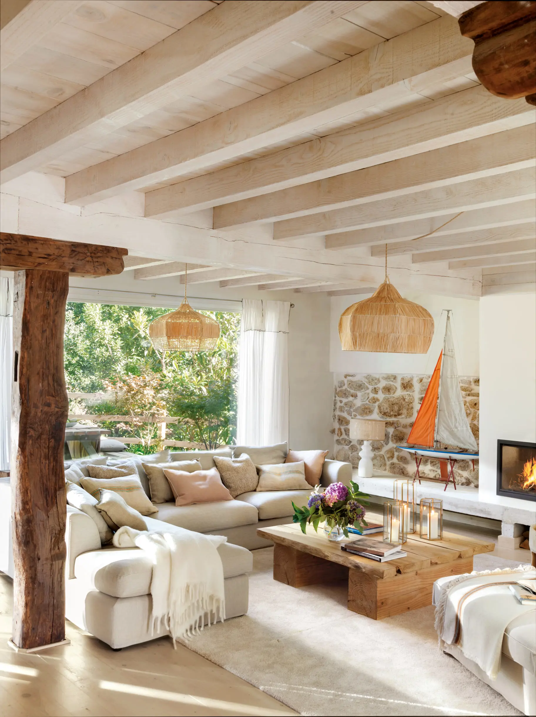 Un salón con sofá esquinero, vigas de madera y chimenea de obra.