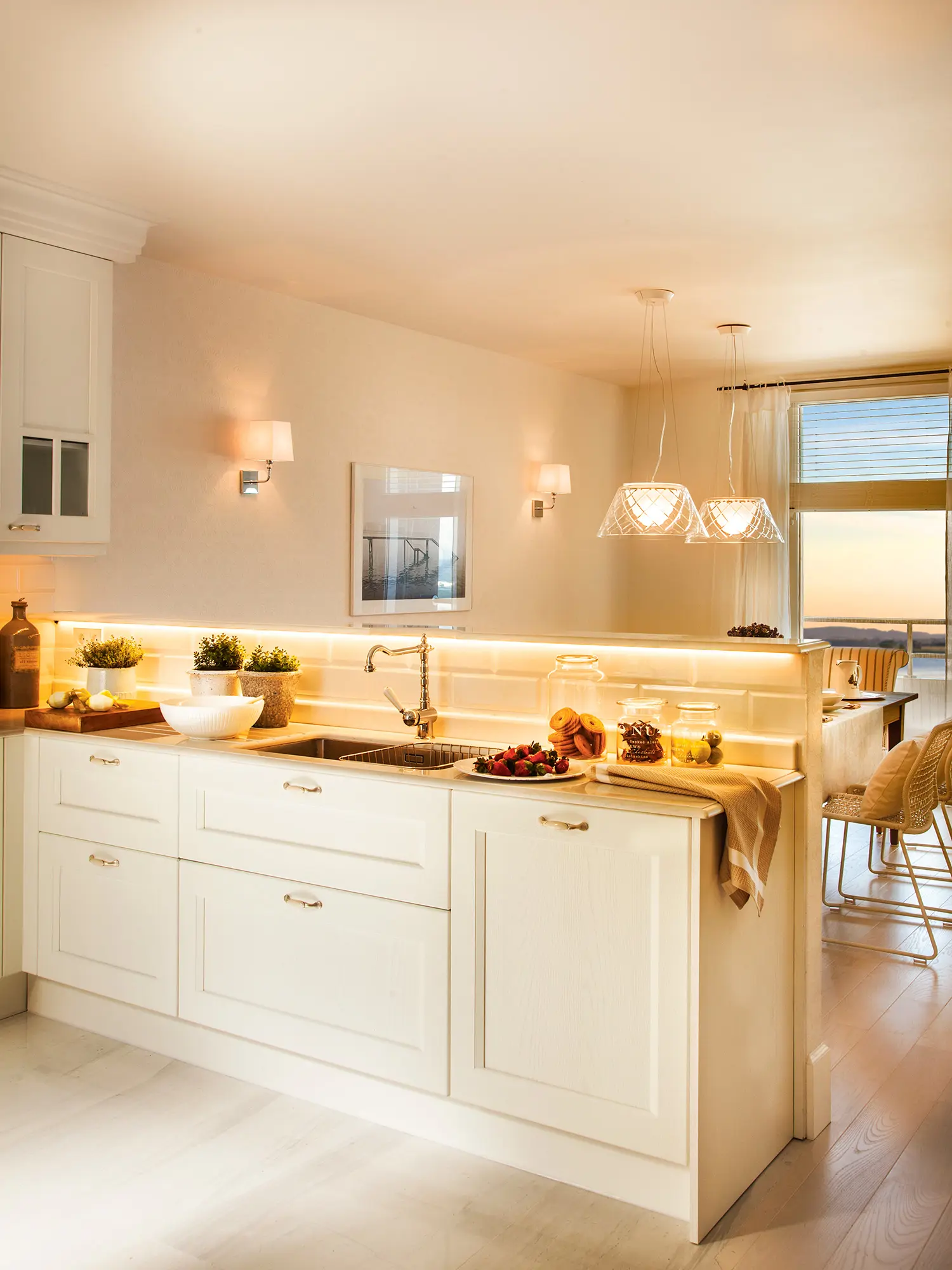 Cocina blanca con tira de led, apliques y lámparas suspendidas en el office