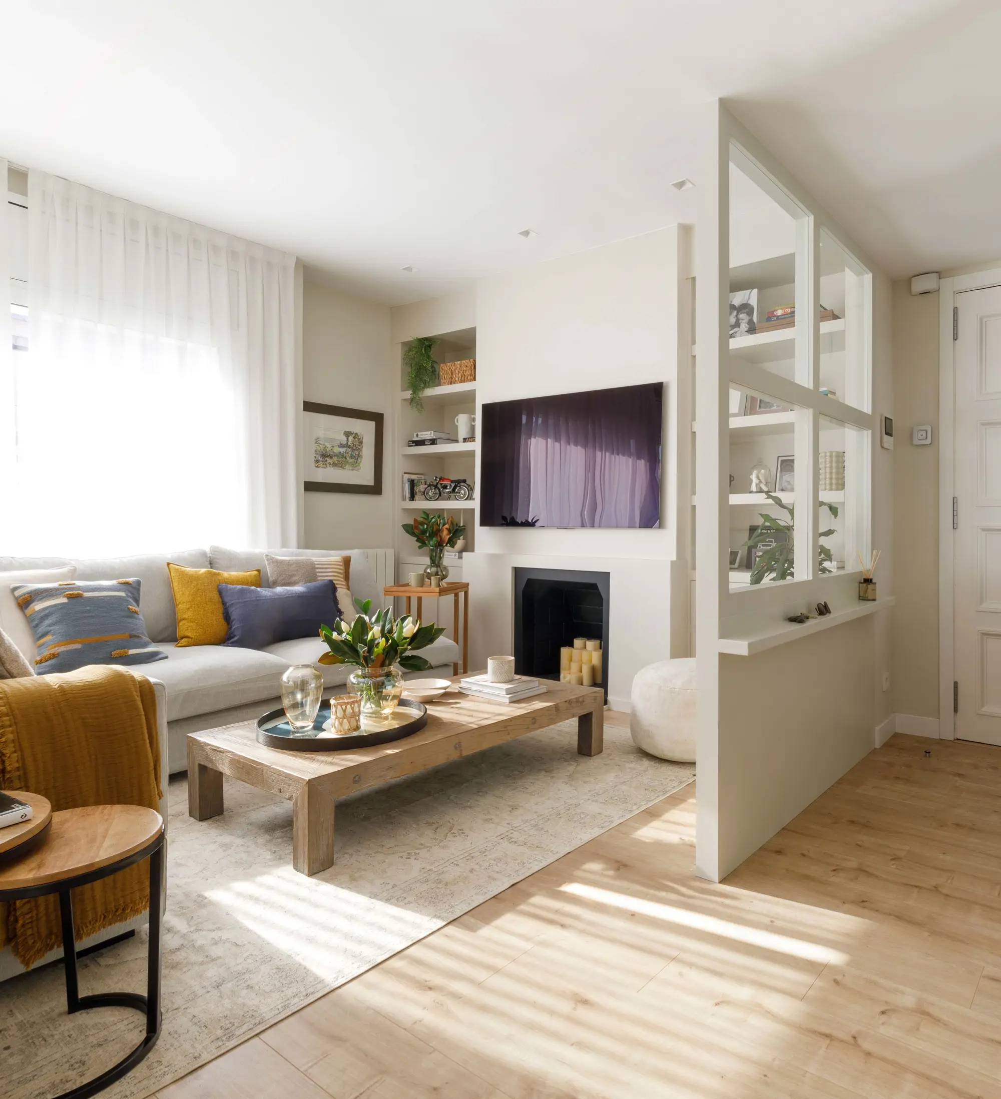 Salón pequeño con chimenea diseñado por Pia Capdevila con cerramiento acristalado que lo separa del recibidor  