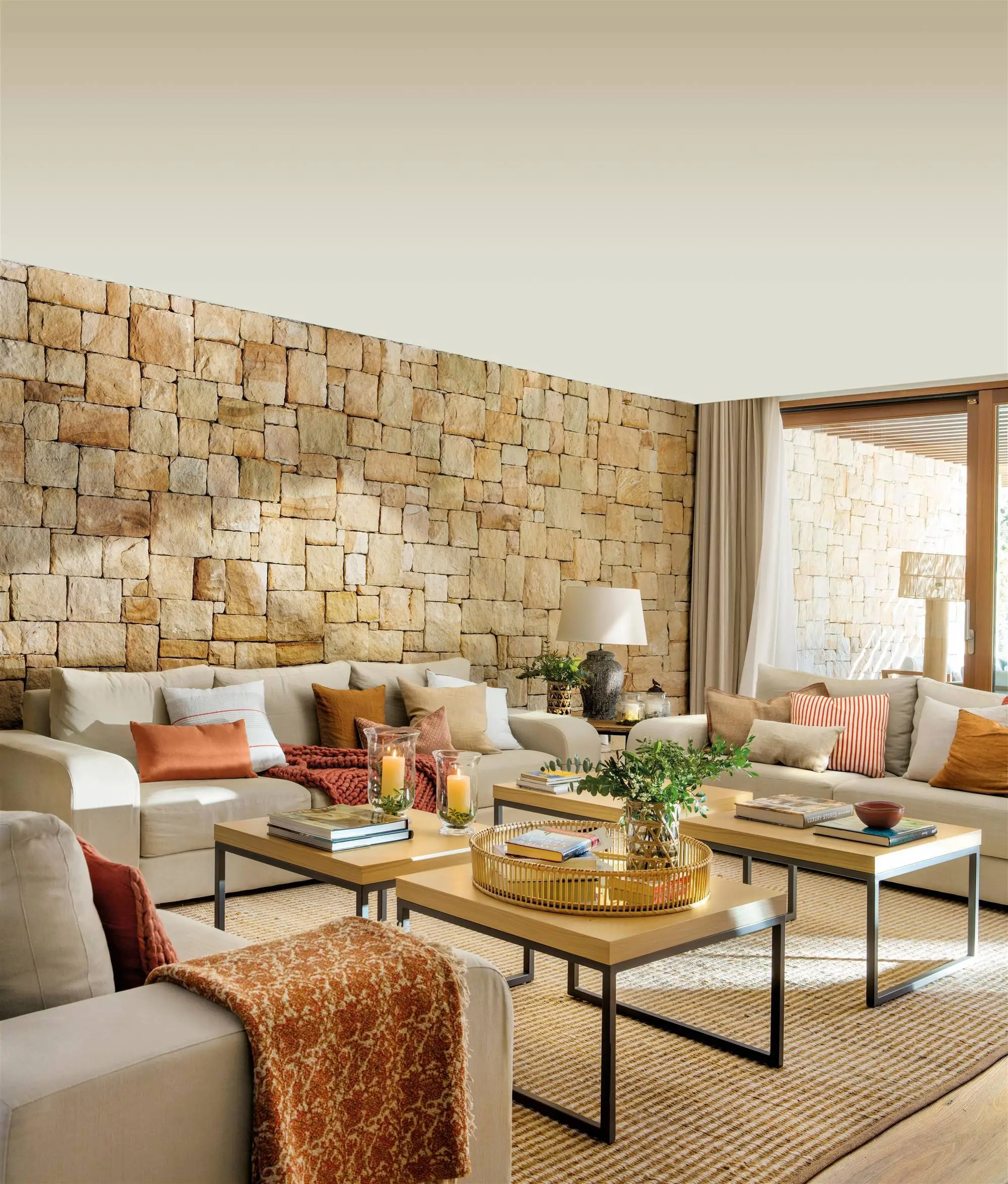 Salón con pared de piedra vista, sofás neutros y mesas de centro de madera.